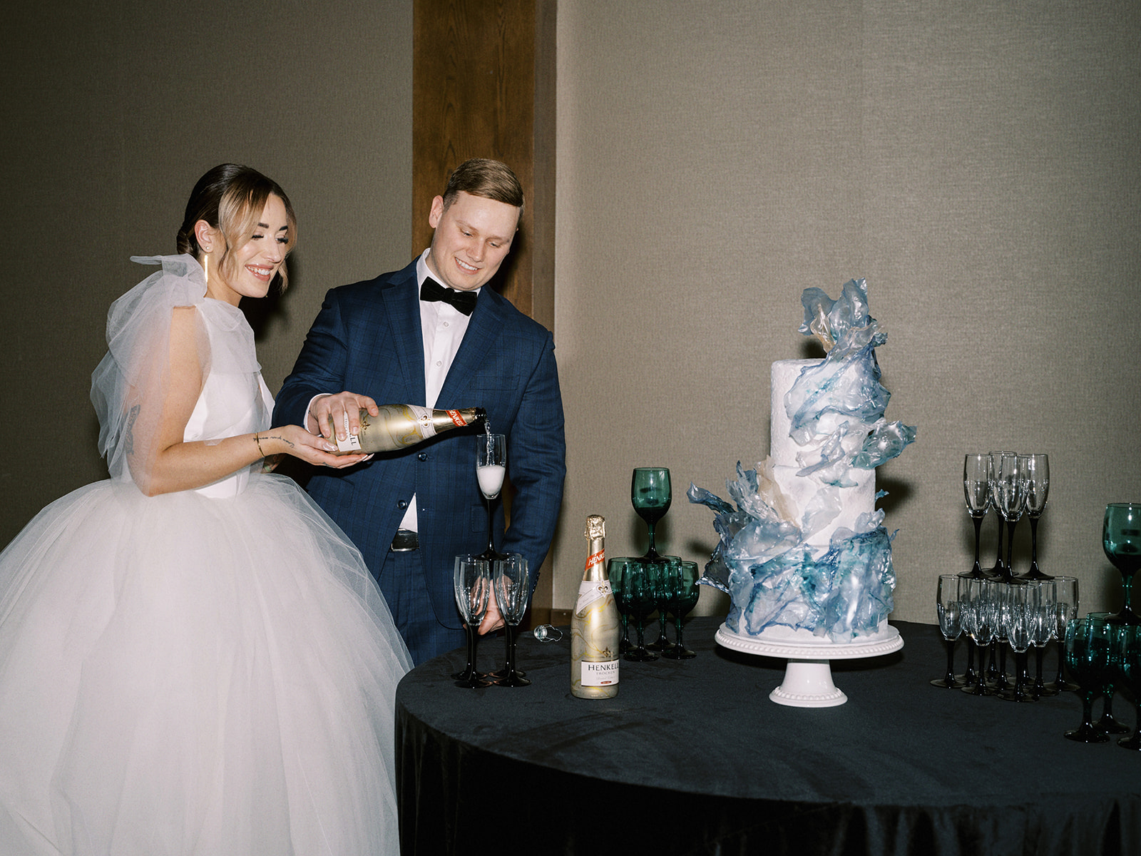 Bride and Groom popping champagne, contemporary and elegant cool-toned wedding cake by Bake My Day at The Malcolm Hotel featuring Mediterranean-inspired decor in oceanic colour palette. 