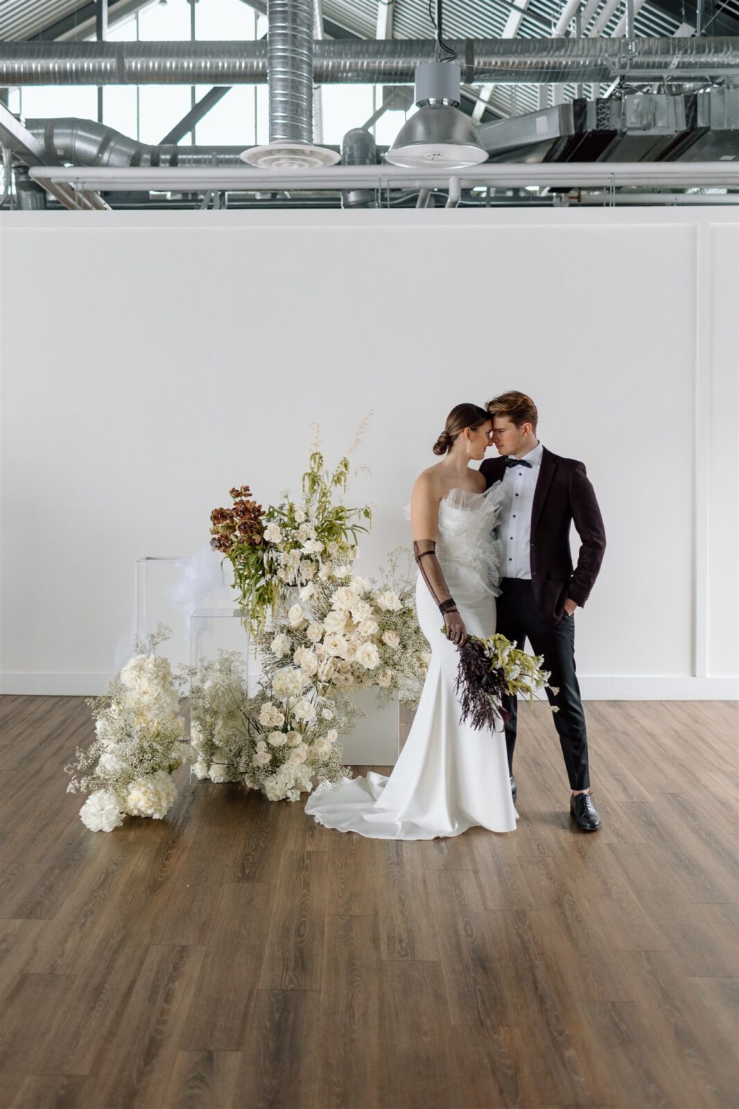 Couple embracing during sophisticated and minimalist wedding at The Wallace Venue in Vancouver, BC. Featuring stunning plum and white florals by Celsia Florals.