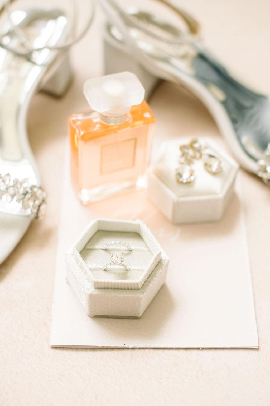 Styled bridal details including designer shoes by Badgley Mischka, peach perfume bottle, white hexagon ring box, and vow book. Spring wedding inspiration.