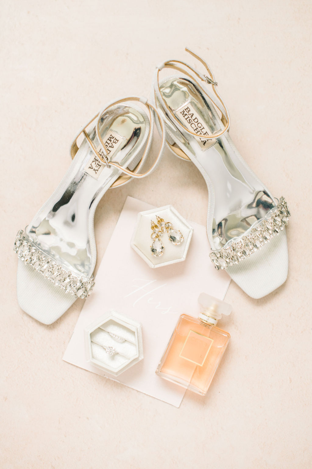 Styled bridal details including designer shoes by Badgley Mischka, peach perfume bottle, white hexagon ring box, and vow book. Spring wedding inspiration.