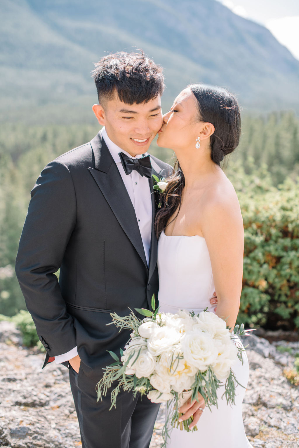 Elegant bride and groom embracing in the mountains of Banff, Alberta. Canadian summer mountain wedding inspiration. Sophisticated mountain bridal portraits by Corrina Walker Photography. 