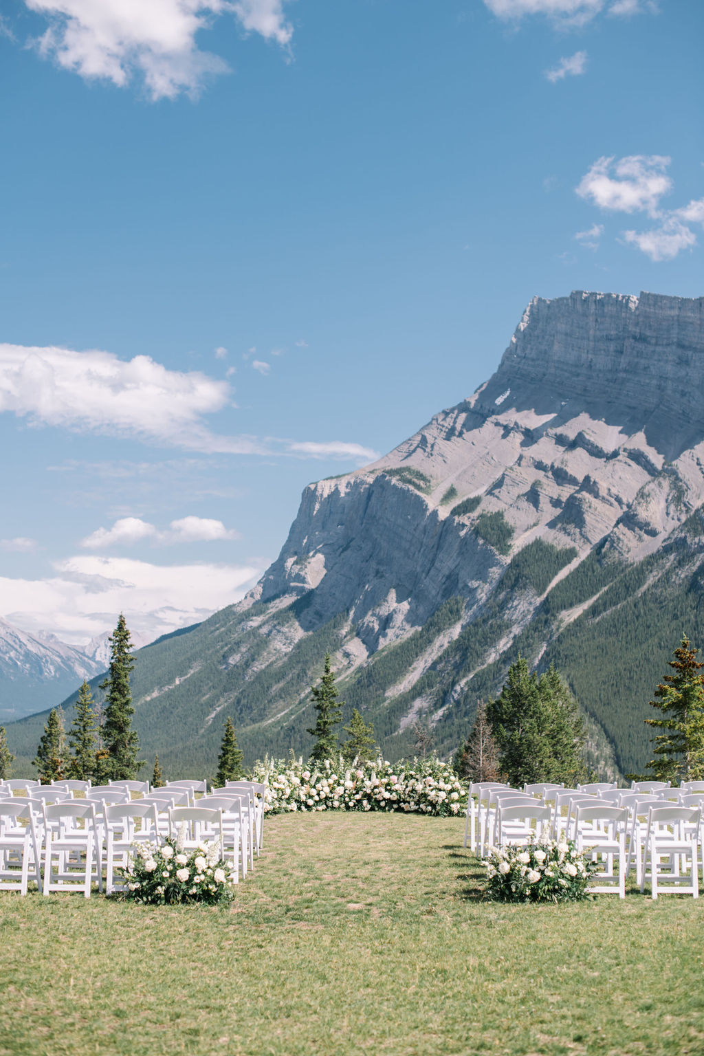 Elegant grounded ceremony floral arch featuring white roses, pink peonies, and greenery by Flowers by Janie. Sophisticated mountain wedding inspiration in Banff, Alberta, Canada. 