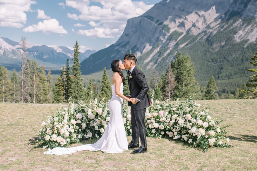 Bride and groom exchange first kiss during sophisticated mountain wedding in Banff, Alberta, Canada. Summer mountain wedding inspiration. 