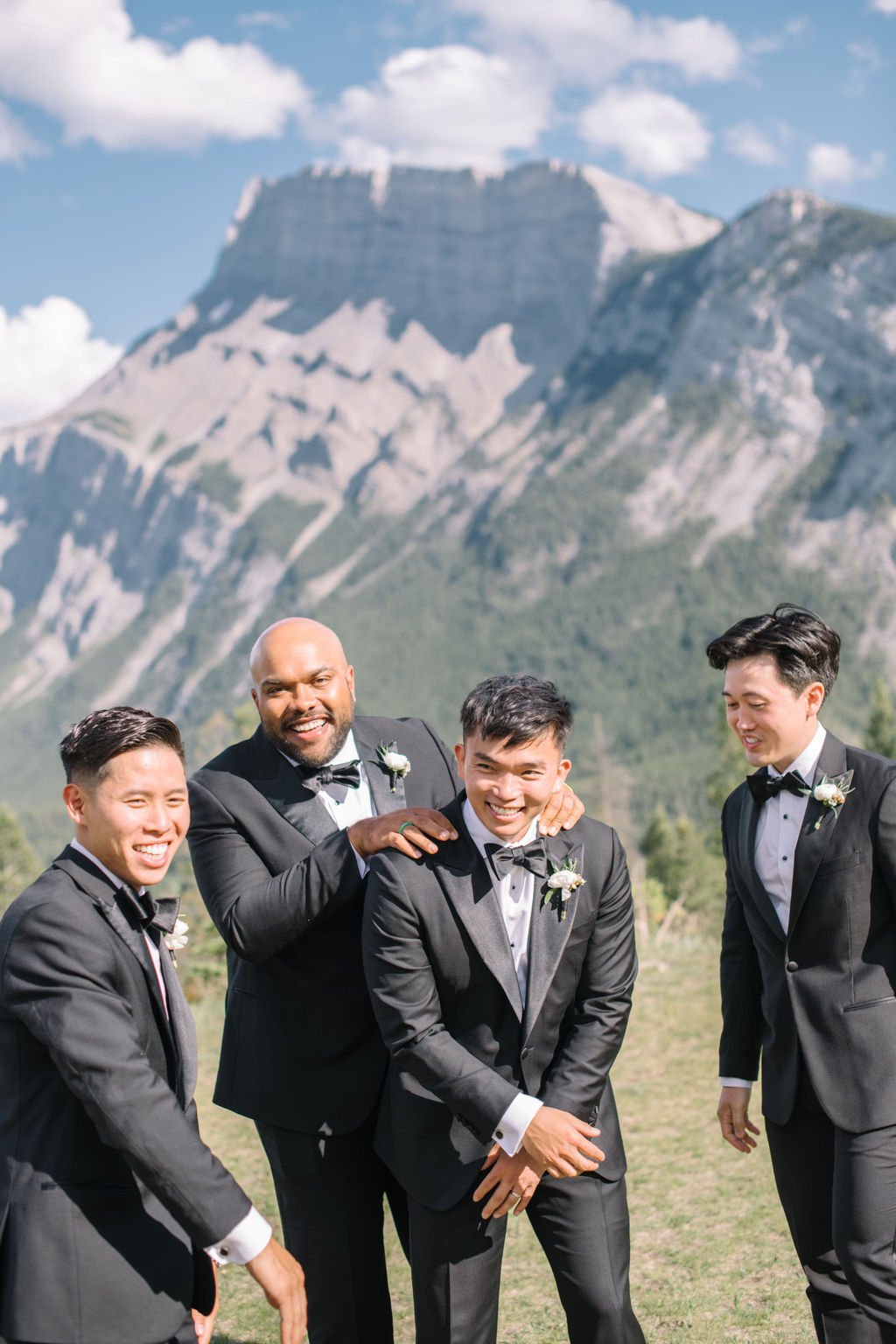 Groom having fun with his groomsmen in the mountains of Banff, Alberta, Canada. Elegant summer wedding inspiration. Classic black suits with white boutonniere. Groom fashion inspiration. 