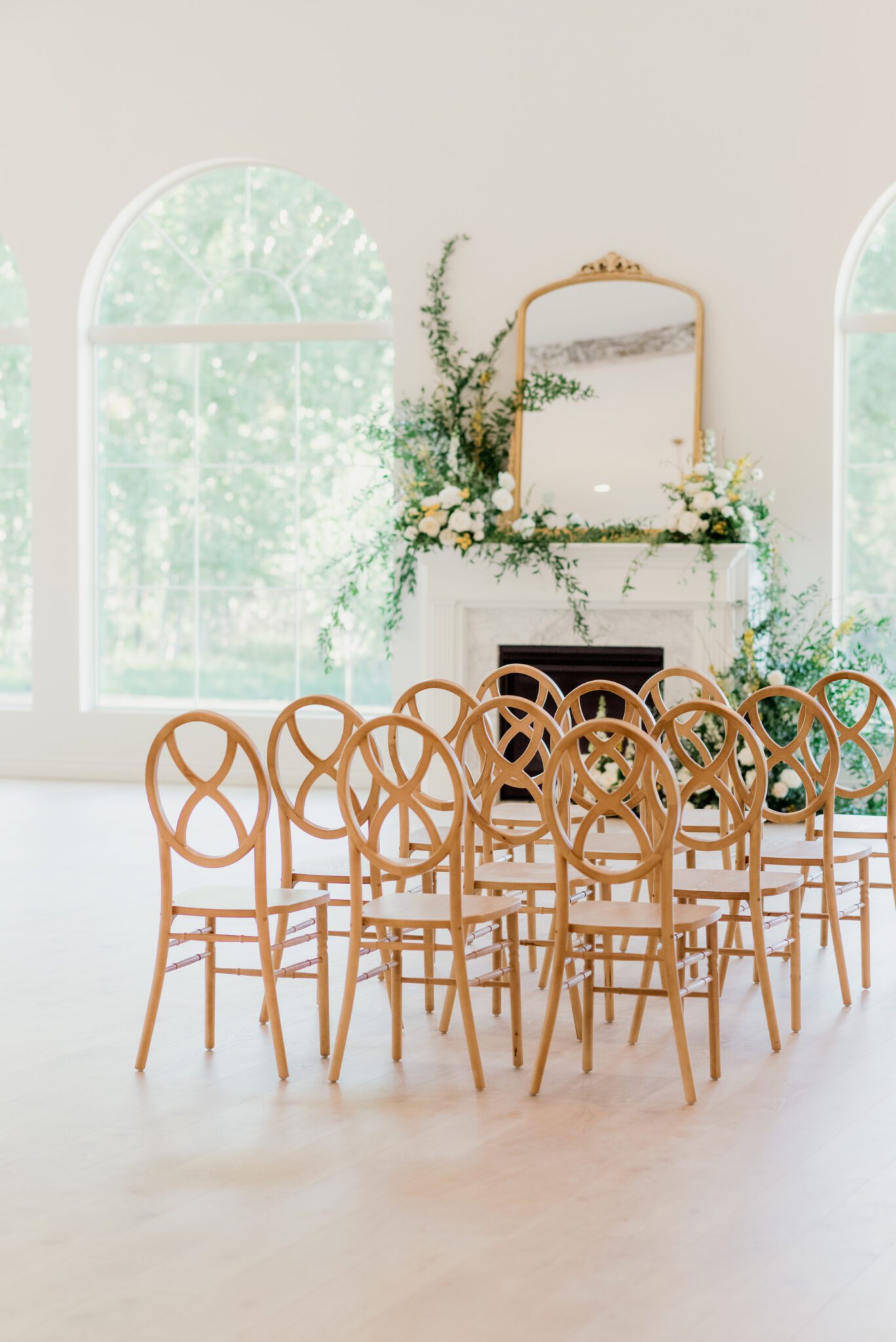 Indoor wedding ceremony at Sparrow Lane with a lush floral installation climbing up the fireplace. Wooden infinity chairs, lush pale yellow, ivory, white, and green fine art wedding colour palette. 