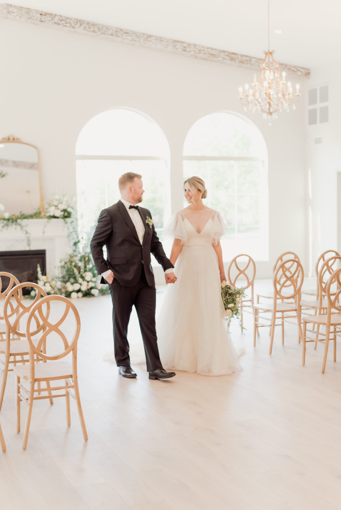 Indoor wedding ceremony at Sparrow Lane with a lush floral installation climbing up the fireplace. Wooden infinity chairs, lush pale yellow, ivory, white, and green fine art wedding colour palette. 