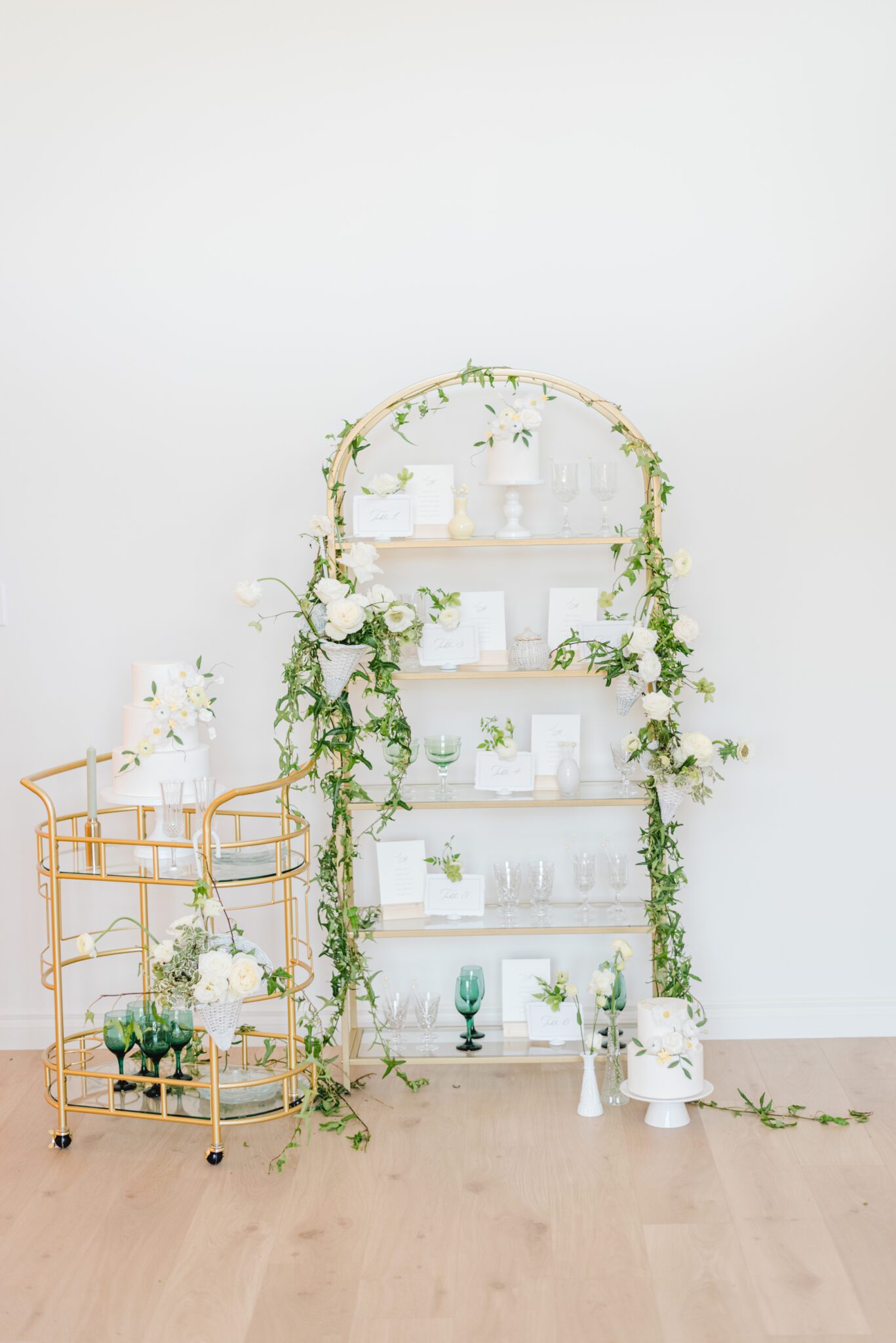 Sophisticated, fine art Spring wedding reception inspiration at Sparrow Lane, gold cart with 3-tiered white wedding cake, elegant gold shelf with custom wedding signage and stationery, styled with cascading pale yellow, ivory and white florals and greenery. 