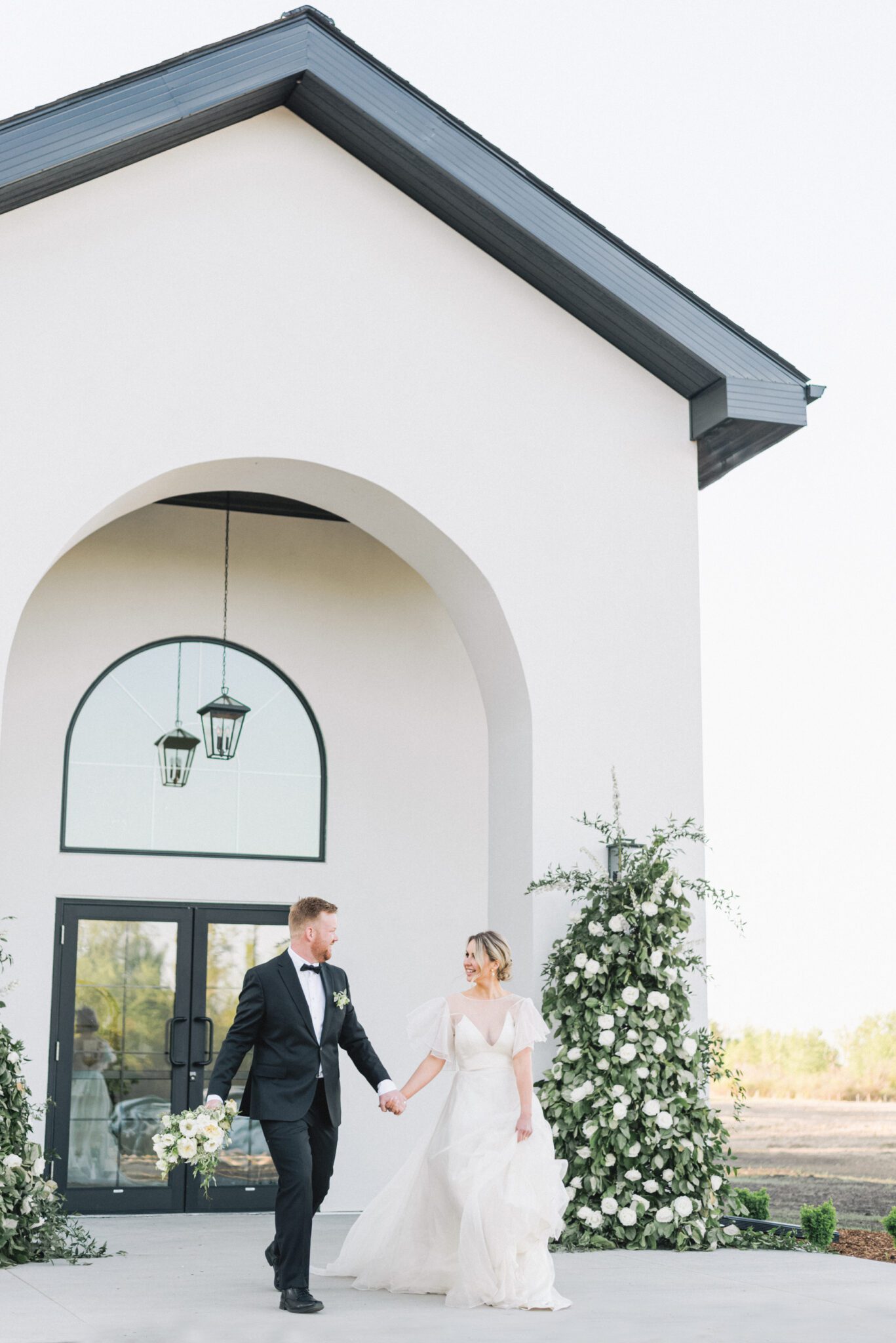Bride and groom embracing in front of Sparrow Lane in Edmonton, Alberta during fine art summer wedding. Pale yellow, ivory, white and green cottage core inspired wedding inspiration. Bride wearing whimsical yet sophisticated bridal gown.