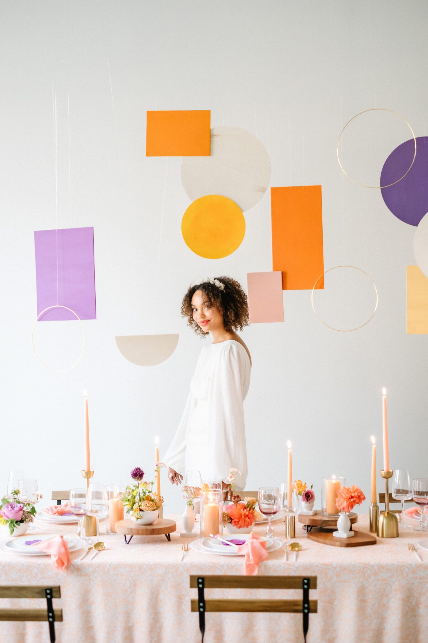 Bright & Colourful Brunch Wedding Inspiration at The Brownstone Calgary, Bronte Bride. Retro inspired vibrant colour palette of purple, orange, yellow, peach, tangerine and coral. Geometric hanging installation over the tables. Bride wearing short bridal gown with long draped sleeves. 