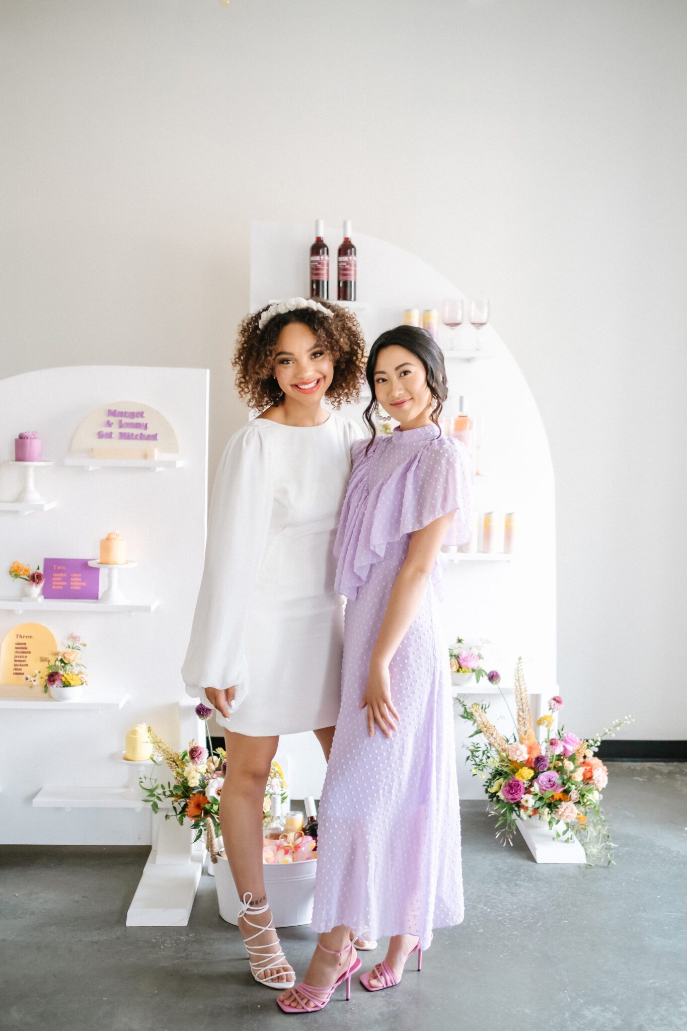 Retro-inspried purple bridesmaid dress, and short bridal gown with flowing sleeve. Bright and colourful wedding at The Brownstone Calgary, brunch wedding inspiration that combines mod style with retro decor. Tangerine, peach, purple and yellow colour scheme. Custom cocktails, retro inspired signage and custom mini wedding cakes.  