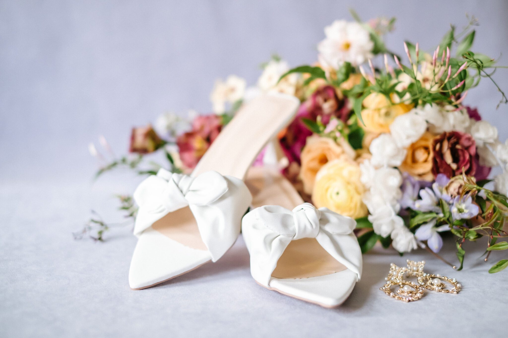 Bridal shoes and earrings paired with Yellow, tangerine, peach, pink, and purple colourful and bold florals by Meadow & Vine at The Brownstone in Calgary, Alberta. 