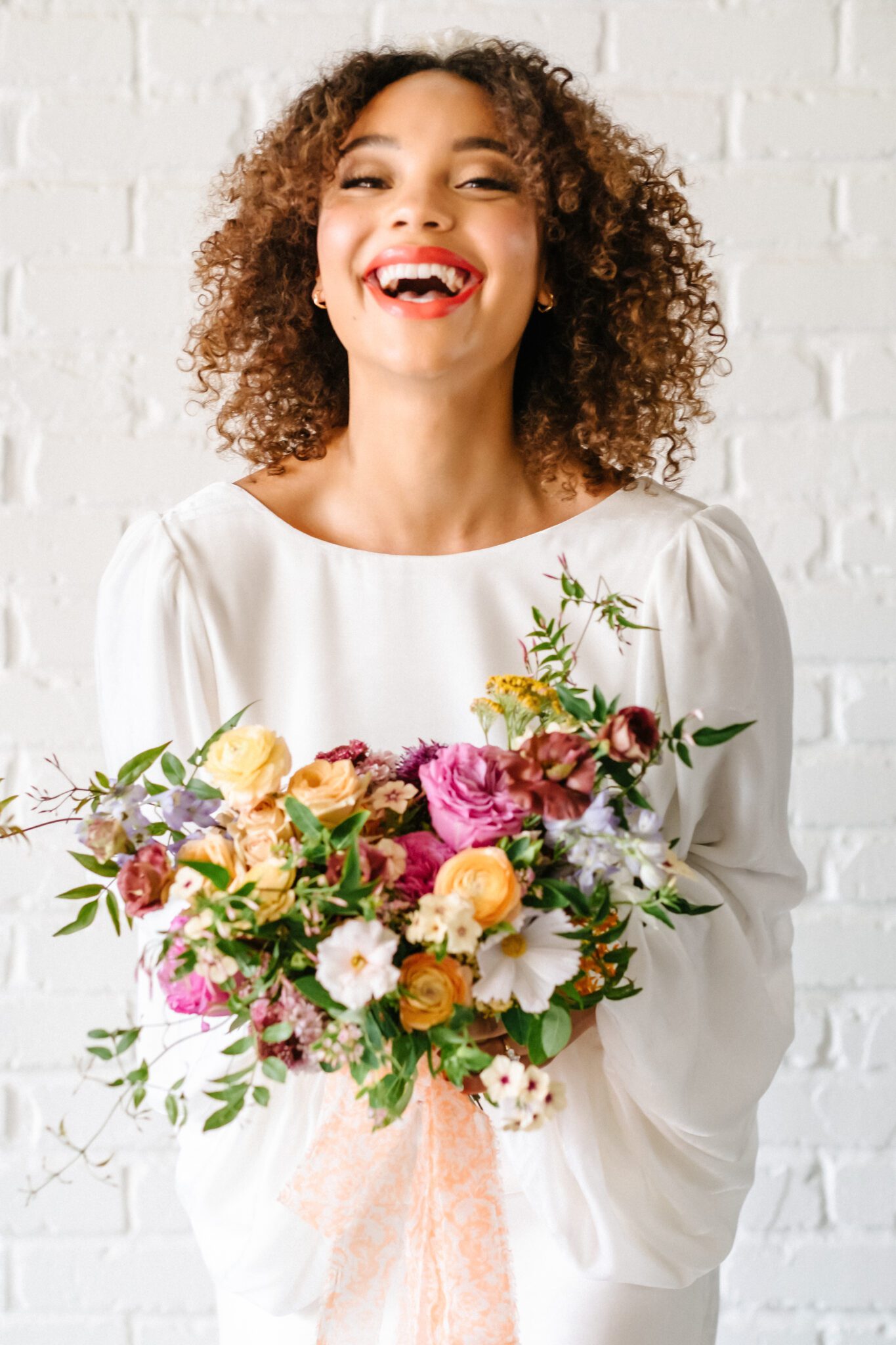 Bright & Colourful Brunch Wedding Inspiration at The Brownstone Calgary, Bronte Bride. Retro inspired vibrant colour palette of purple, orange, yellow, peach, tangerine and coral. Bride wearing short bridal gown with long draped sleeves, holding colourful floral bouquet by Meadow & Vine