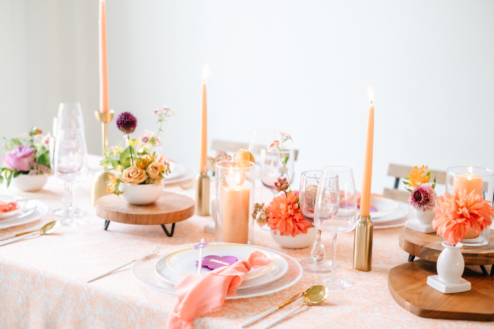 Bright & colourful brunch wedding tablescape. Florals by Meadow & Vine. Retro-inspired vibrant colour palette of purple, orange, yellow, peach, tangerine and coral. Wood and gold accents. Custom retro purple flower name place card. 