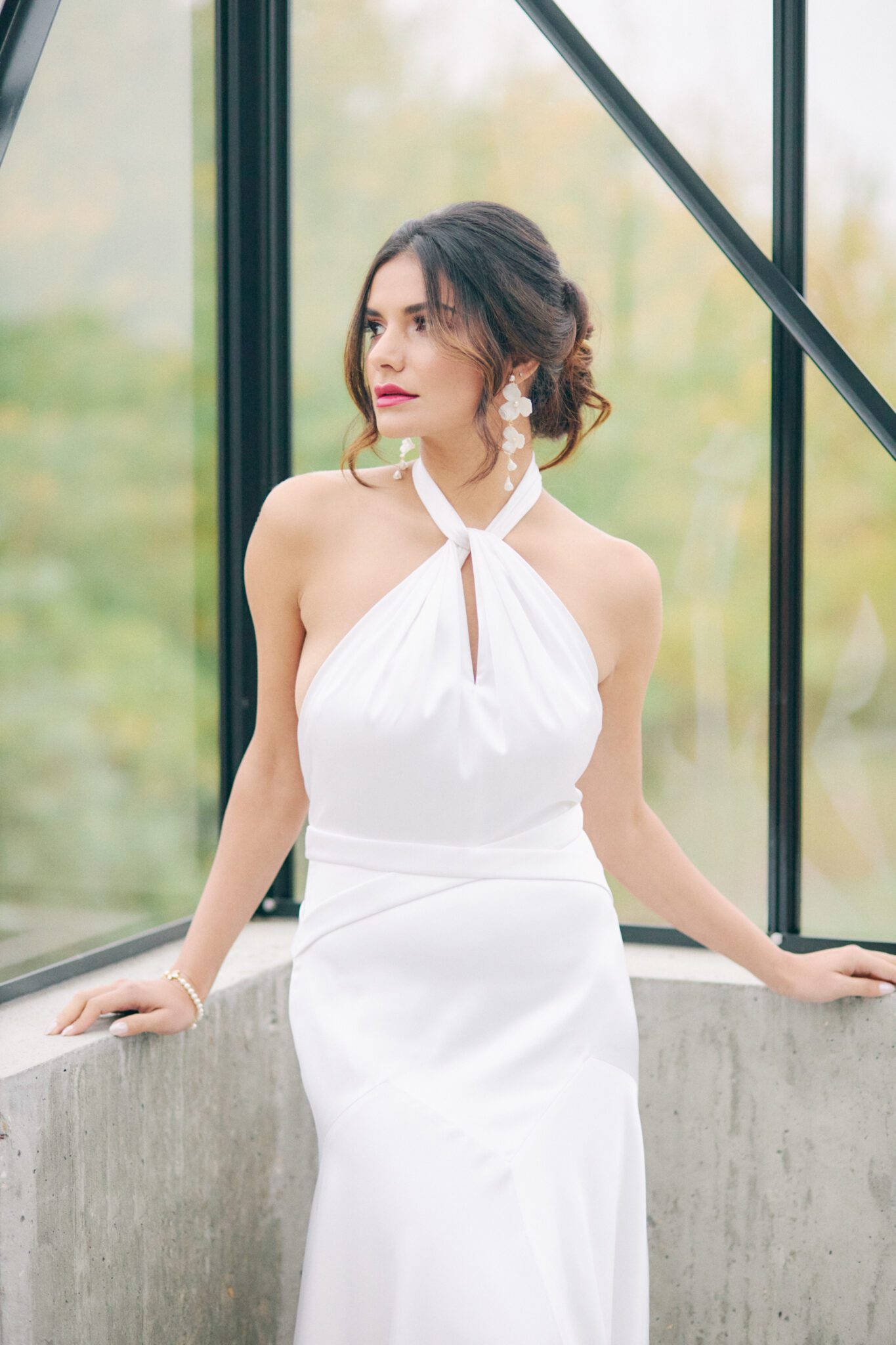 Elegant and modern bride wears a halter style wedding dress, pearl hairpiece, and statement earrings by Joanna Bisley Designs. Bridal fashion inspiration. 