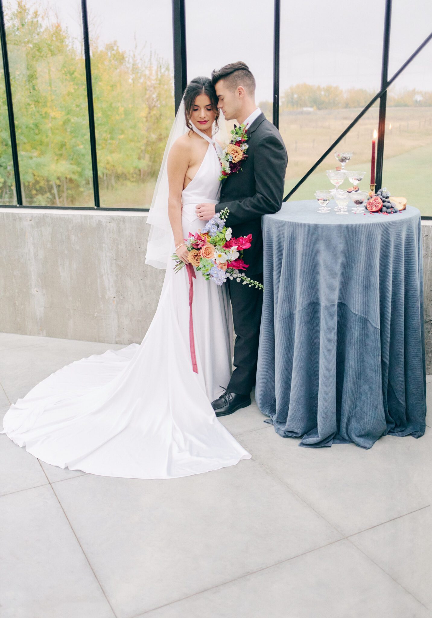 Couple standing in front of elegant champagne tower with fruit details. Vibrant and bold wedding inspiration. Blur corduroy linens and burgundy candles with hints of gold detail. 