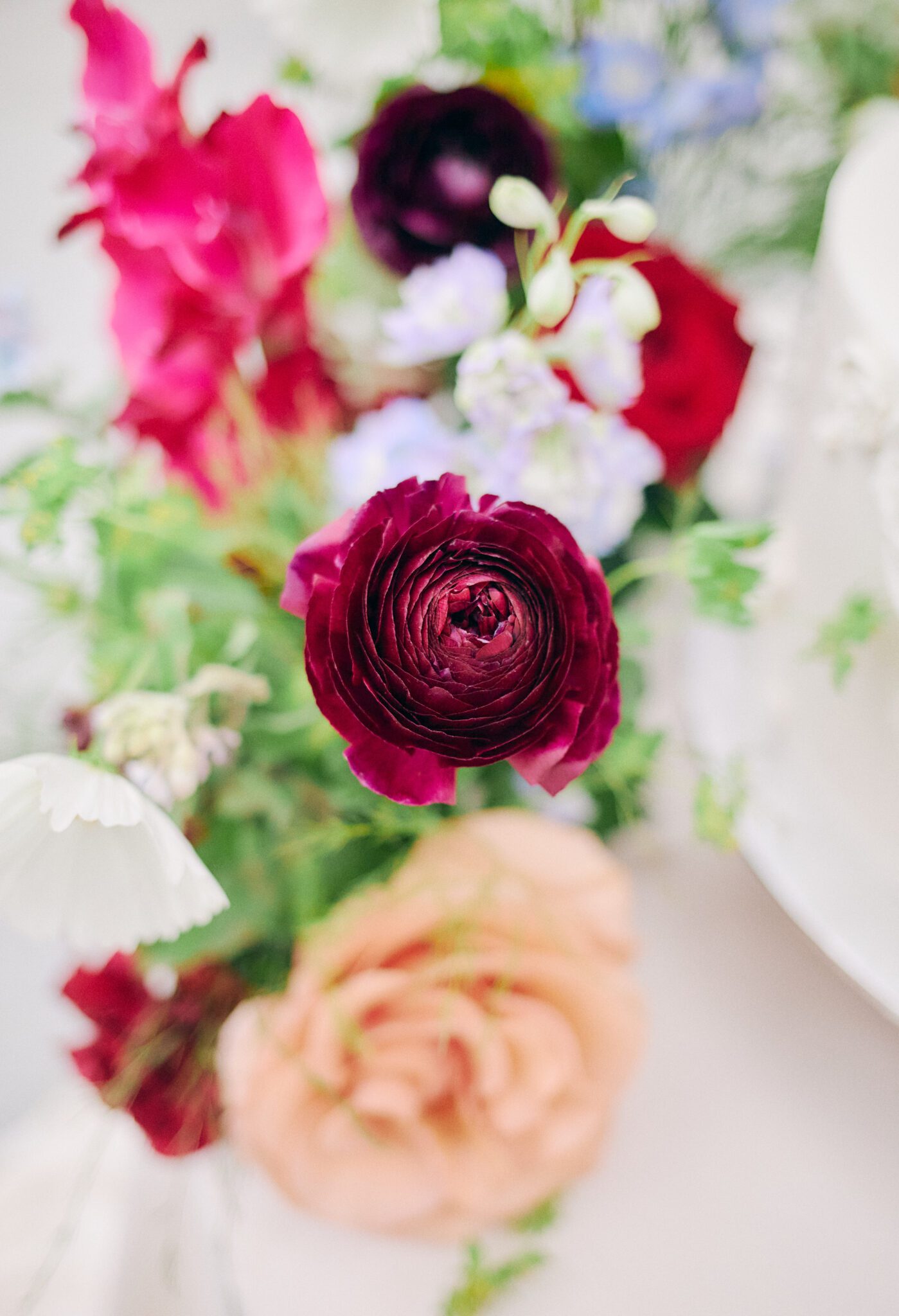 Wedding reception tablescape featuring vibrant flowers in pink, peach, violet, and red, blue corduroy linens, colorful candles with hints of gold, and fruit. Floating floral arch framing the intimate reception space.