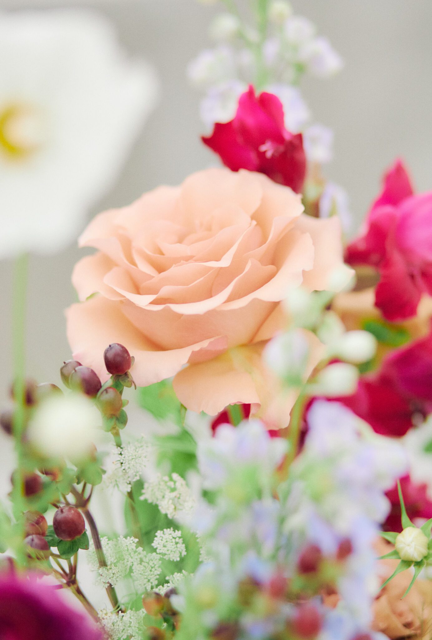 Wedding reception tablescape featuring vibrant flowers in pink, peach, violet, and red, blue corduroy linens, colorful candles with hints of gold, and fruit. Floating floral arch framing the intimate reception space.