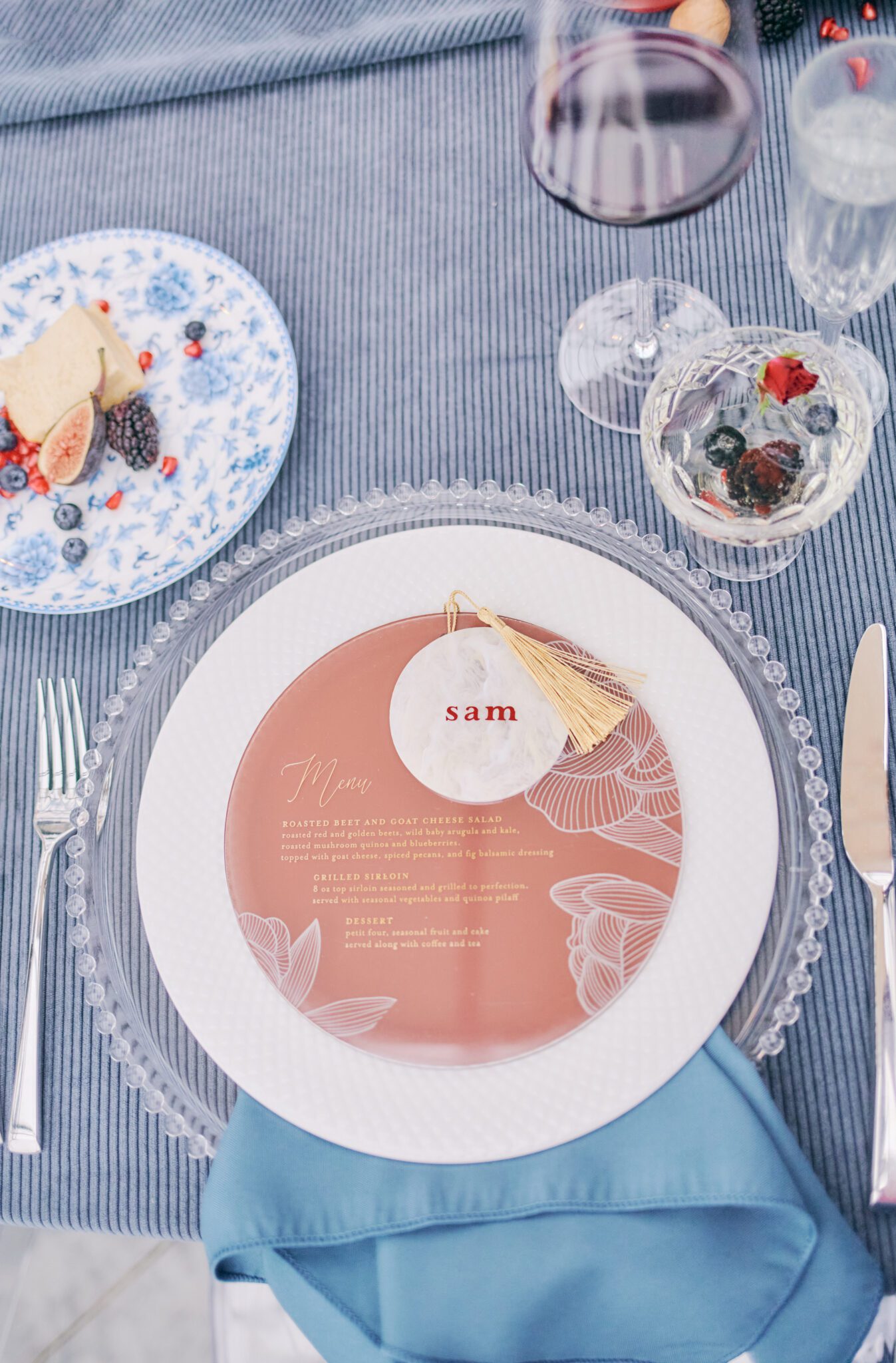 Wedding reception tablescape featuring vibrant flowers in pink, peach, violet, and red, blue corduroy linens, colorful candles with hints of gold, and fruit. Floating floral arch framing the intimate reception space.