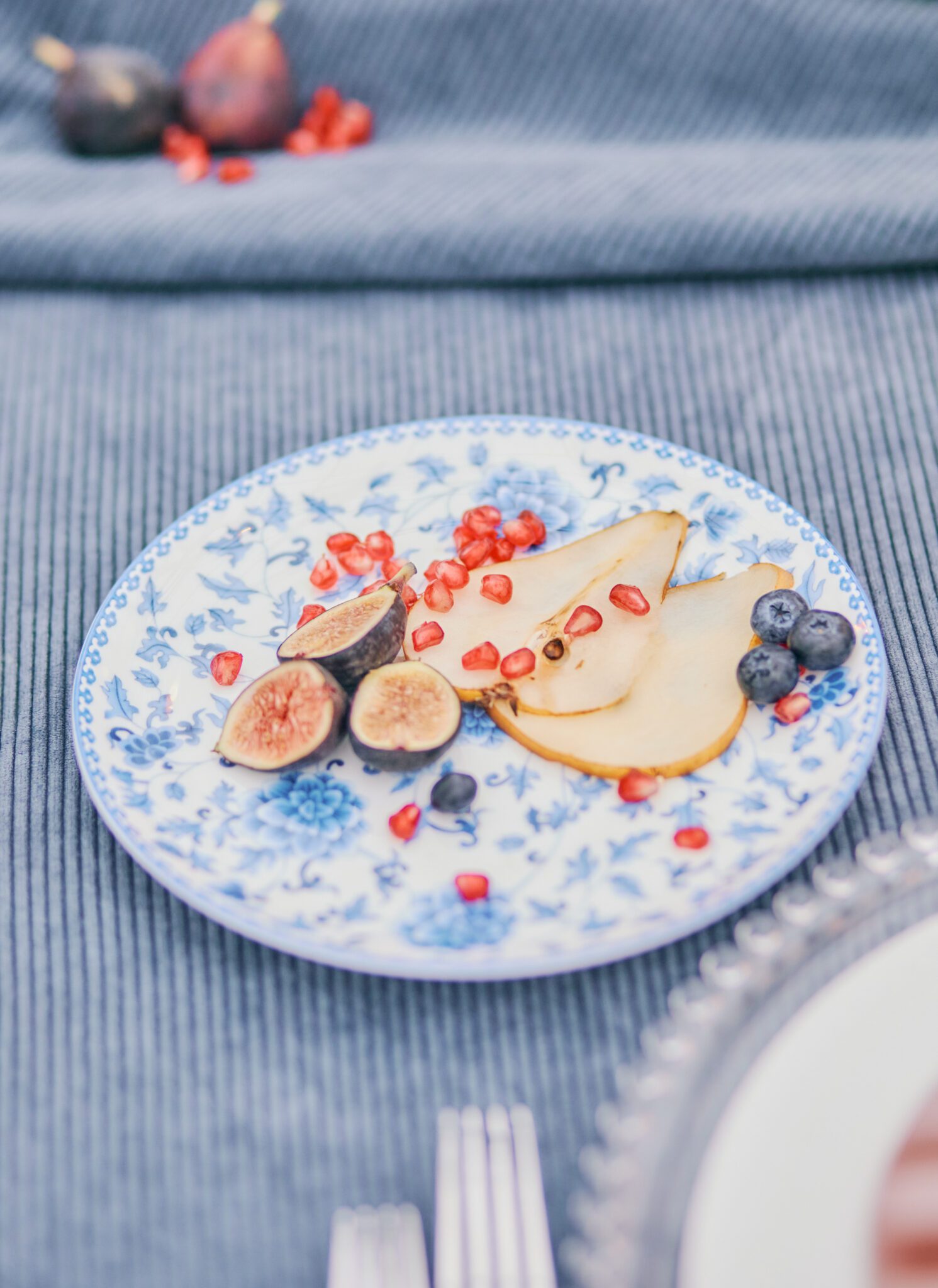 Wedding reception tablescape featuring blue corduroy linens, antique blue and white floral dinnerware and fruit. 