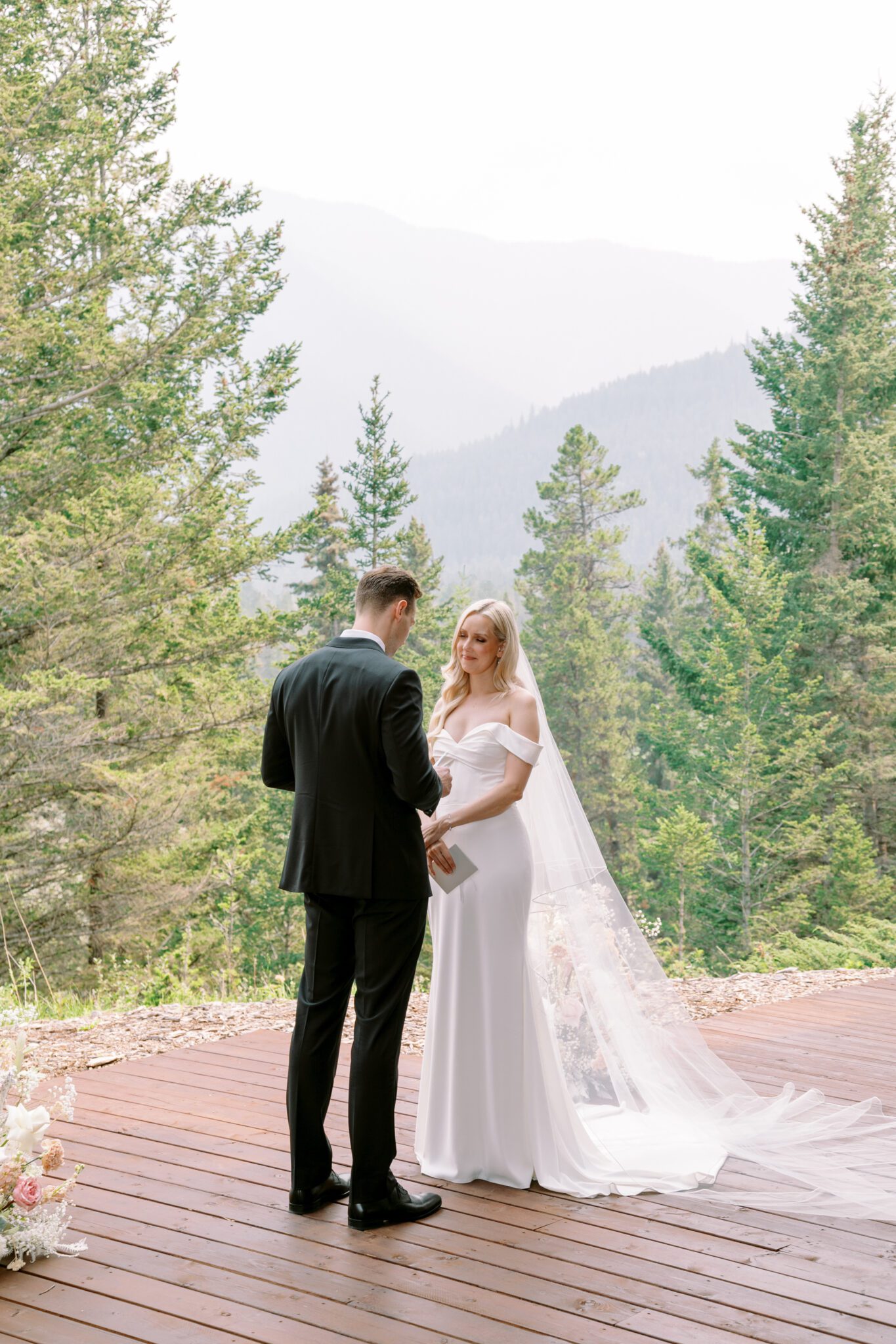 Bride and groom during wedding ceremony at Stewart Creek Golf Course in Canmore, Alberta. White, peach and pink florals. Mountain wedding ceremony. 