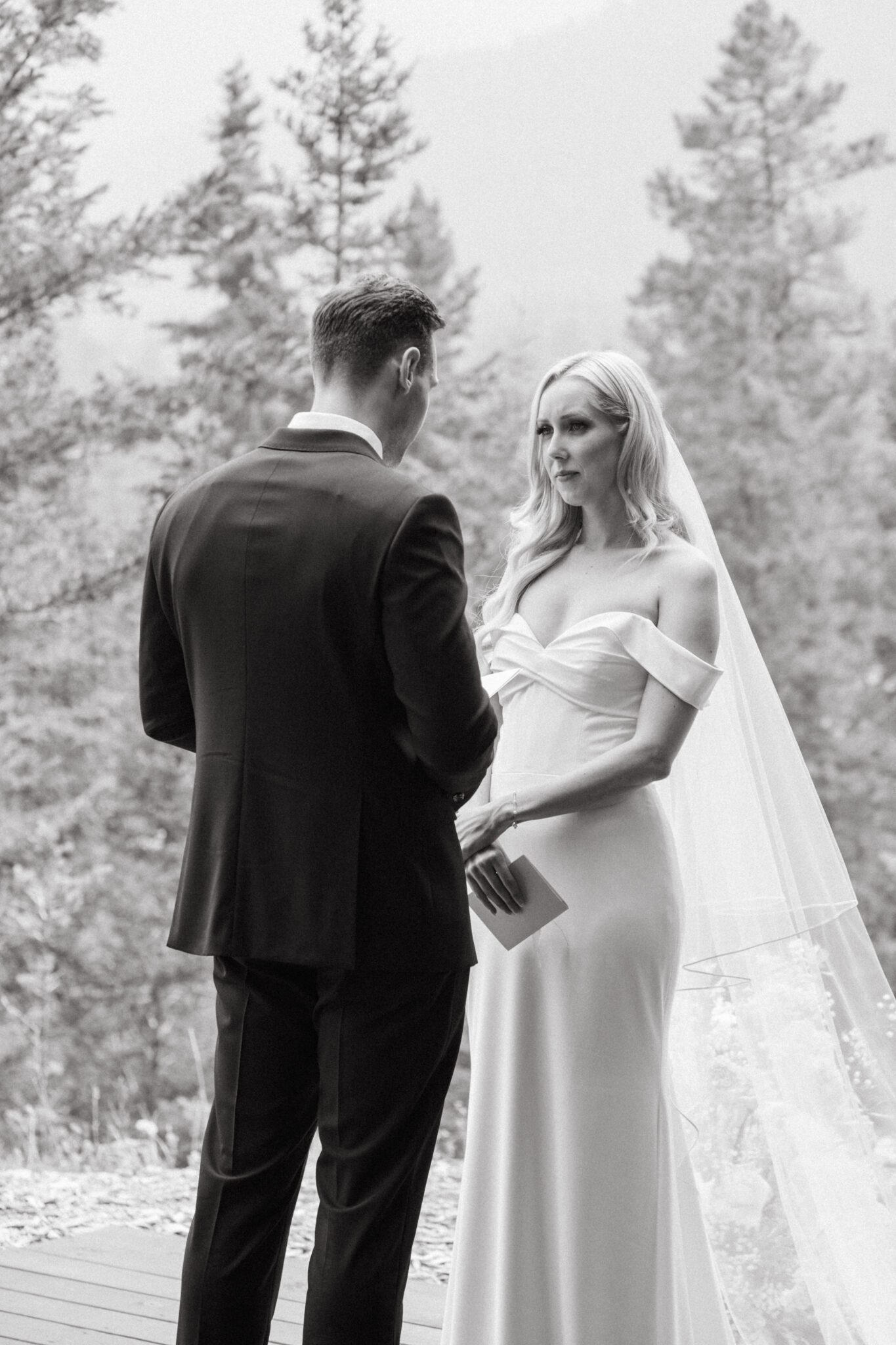 Bride and groom during wedding ceremony at Stewart Creek Golf Course in Canmore, Alberta. White, peach and pink florals. Mountain wedding ceremony. 