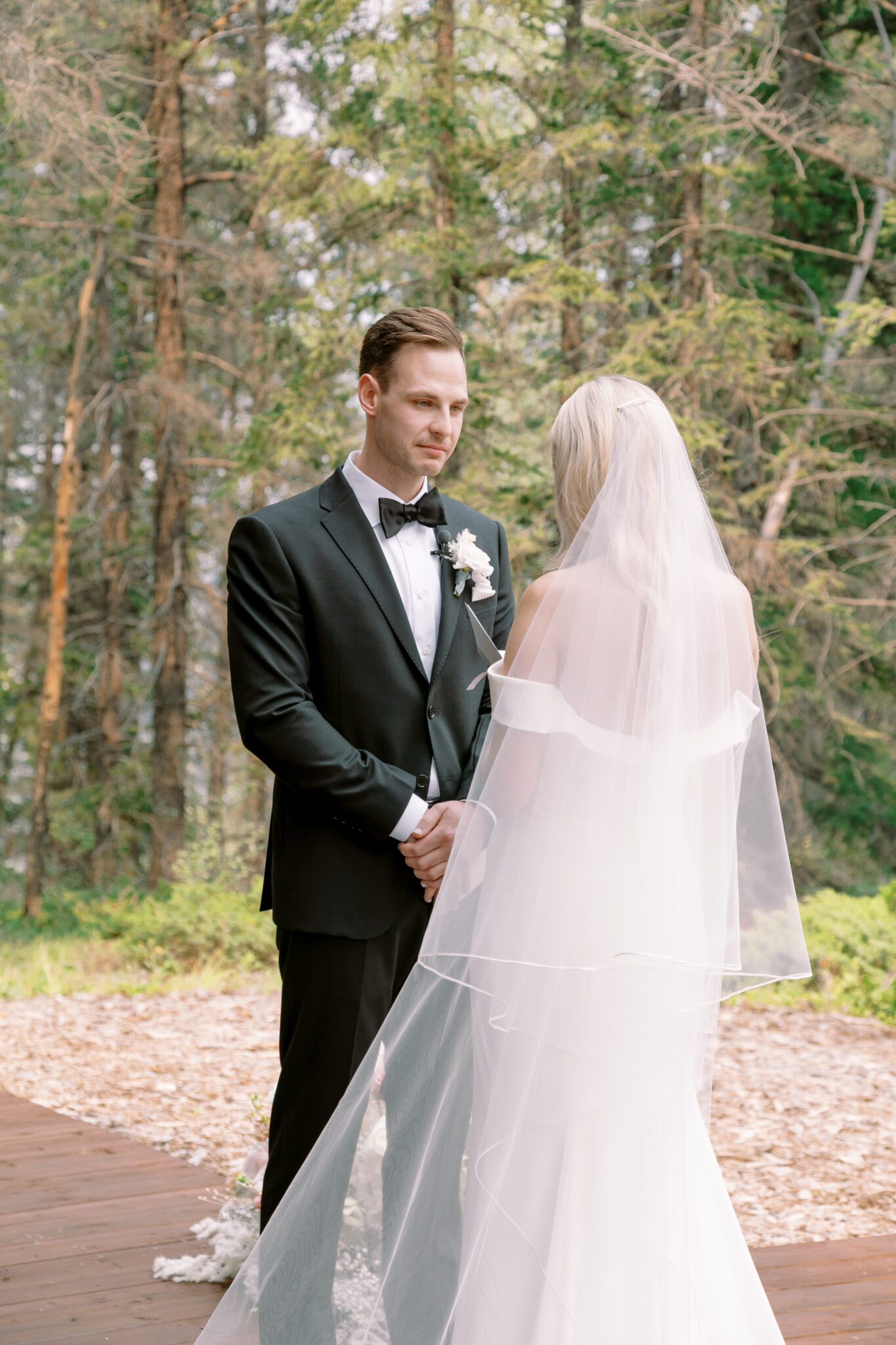 Bride and groom during wedding ceremony at Stewart Creek Golf Course in Canmore, Alberta. White, peach and pink florals. Mountain wedding ceremony. 