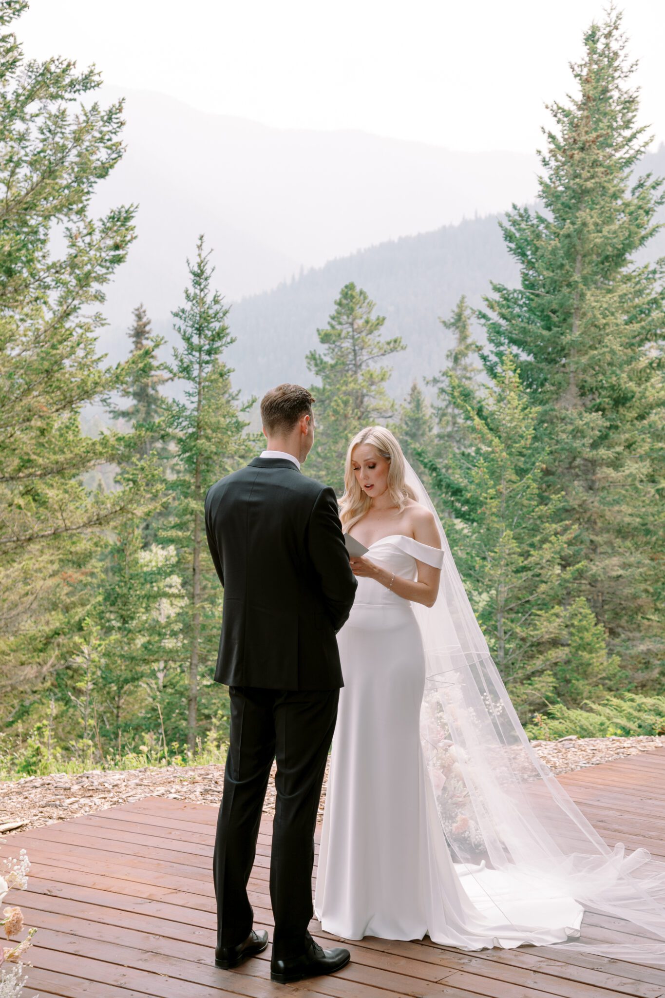 Bride and groom during wedding ceremony at Stewart Creek Golf Course in Canmore, Alberta. White, peach and pink florals. Mountain wedding ceremony. 