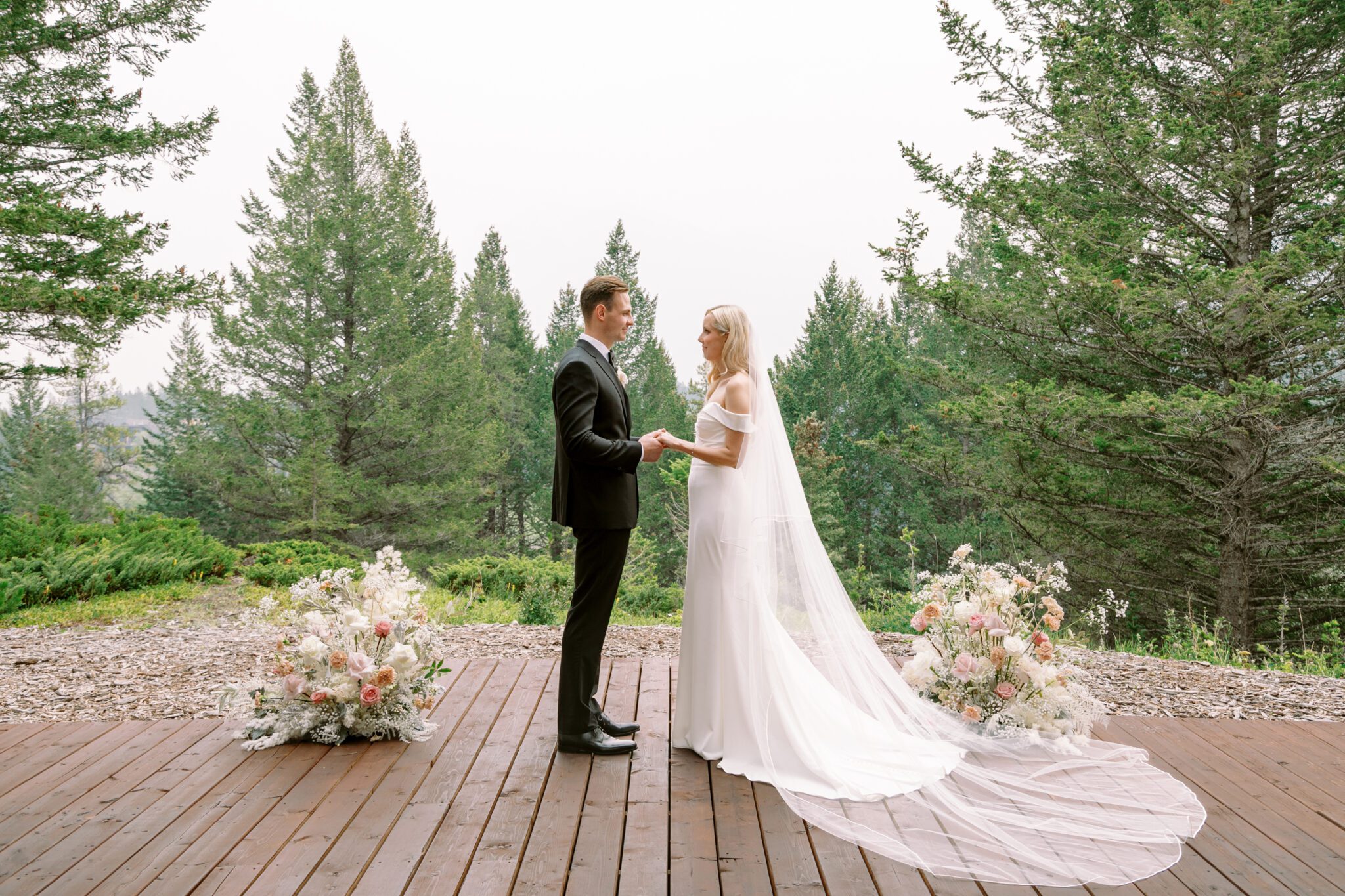 Bride and groom during wedding ceremony at Stewart Creek Golf Course in Canmore, Alberta. White, peach and pink florals. Mountain wedding ceremony. 