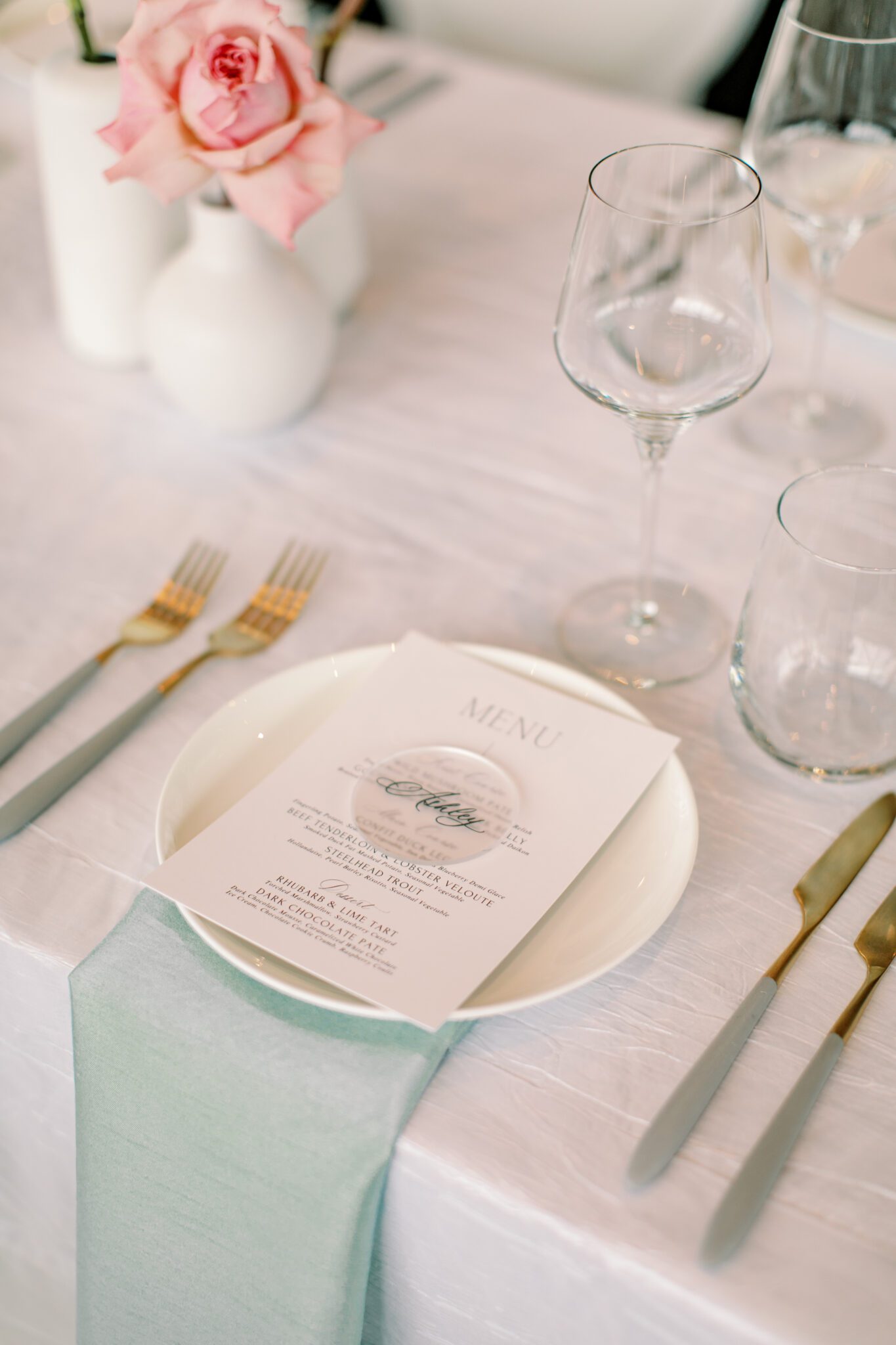 Modern and chic wedding reception at The Sensory in Canmore, Alberta.  Long tables with white linens, blue napkins, and pink floral centrepieces. Gold dinnerware with custom menu.