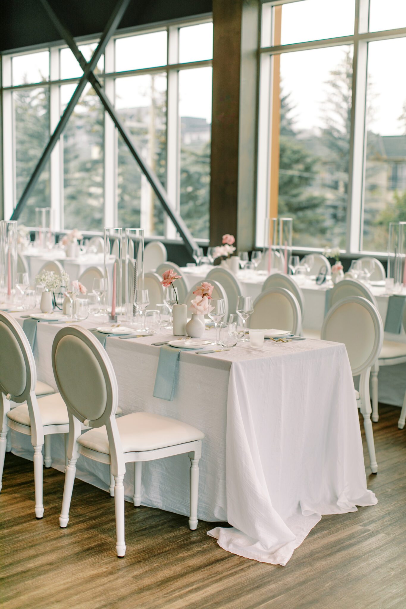 Modern and chic wedding reception at The Sensory in Canmore, Alberta.  Long tables with white linens, blue napkins, and pink floral centrepieces
