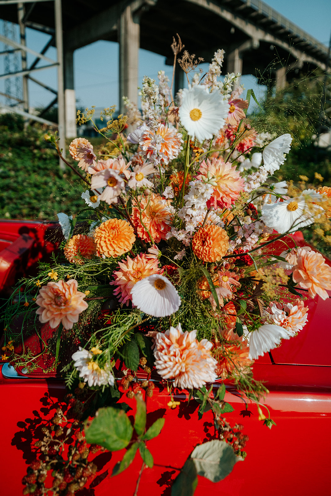 Vintage red muscle car convertible covered in bright and bold summer florals in white, tangerine, red, peach, and pink. South Vancouver feminine meets rock and roll styled shoot. Vintage wedding inspiration. 