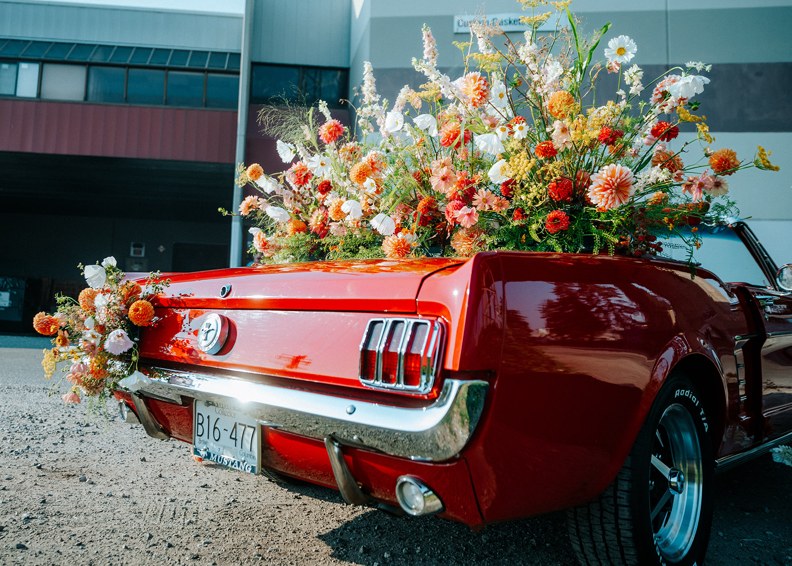 Vintage red muscle car convertible covered in bright and bold summer florals in white, tangerine, red, peach, and pink. South Vancouver feminine meets rock and roll styled shoot. Vintage bold summer wedding inspiration. 