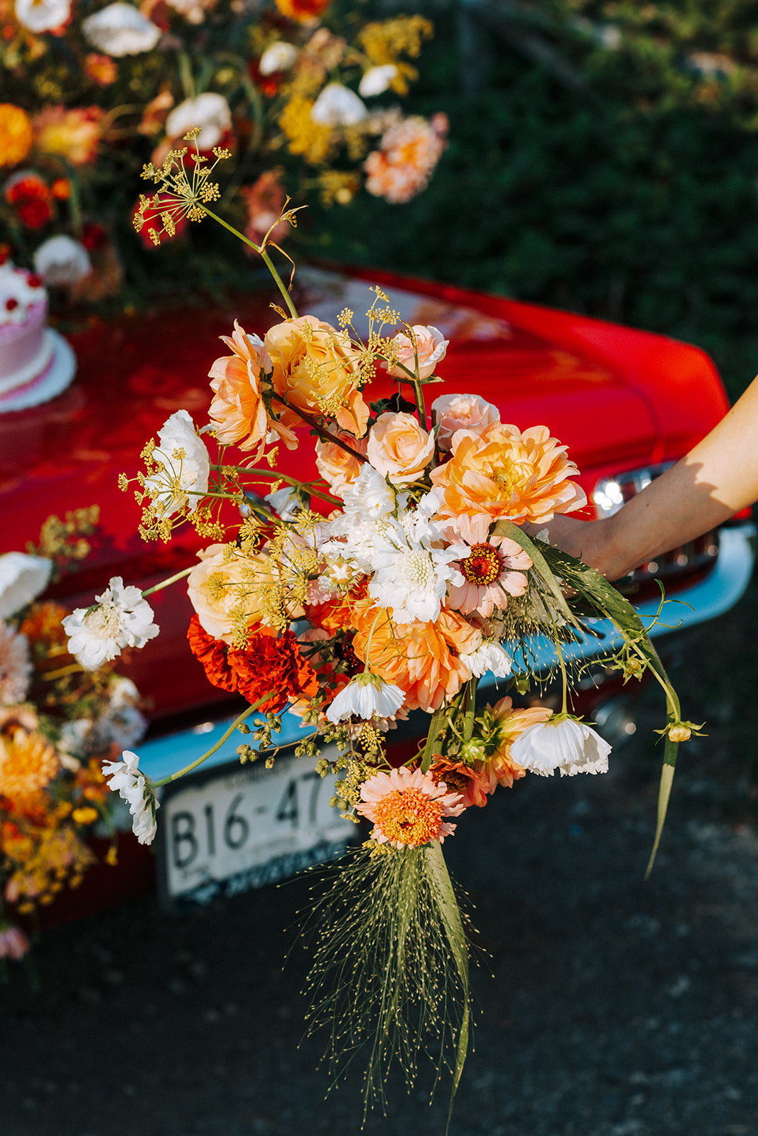 Bouquet of bright and bold summer florals in white, tangerine, red, peach, and pink, with vintage red muscle car in the background. South Vancouver feminine meets rock and roll styled shoot. Vintage wedding inspiration. 