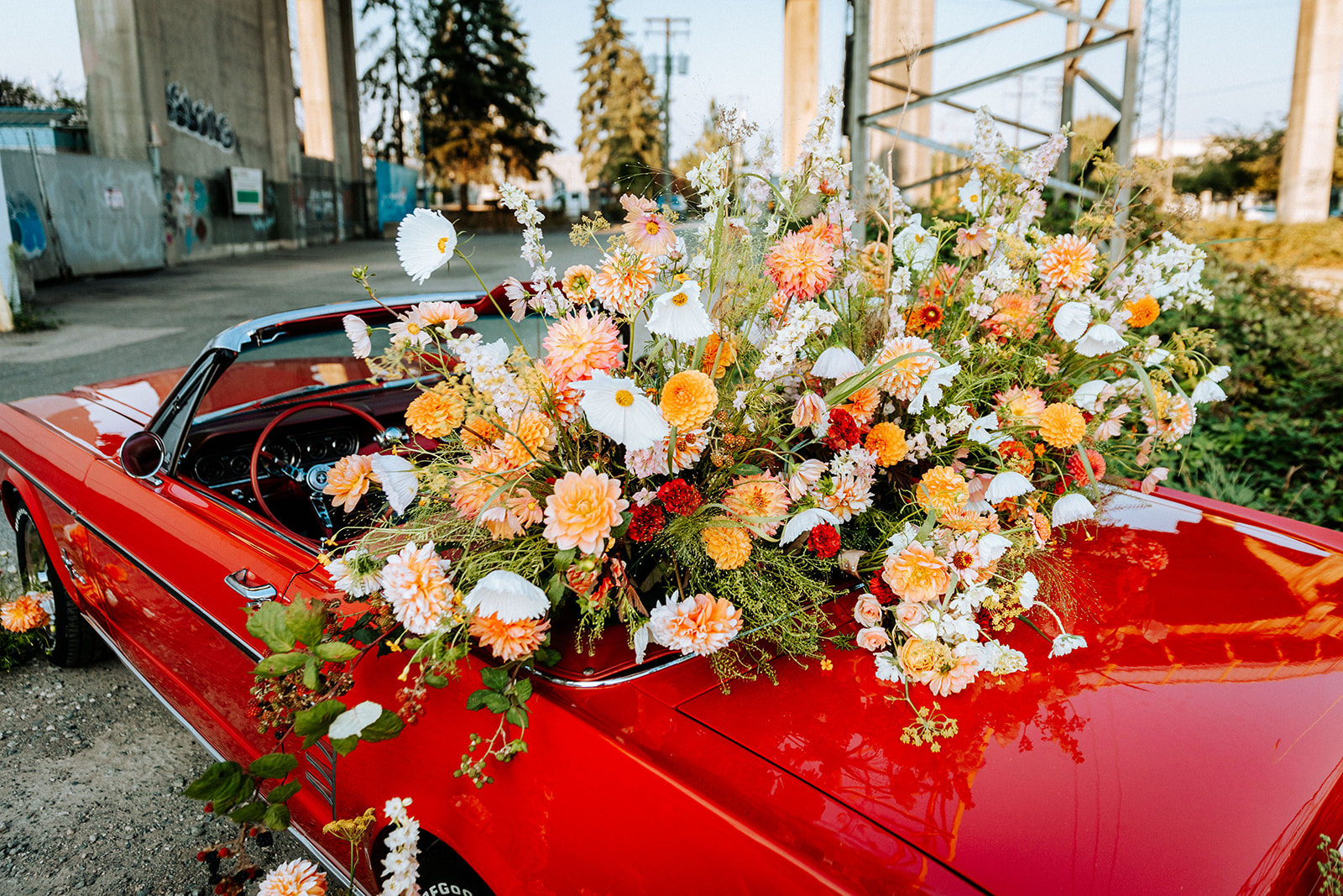 Vintage red muscle car convertible covered in bright and bold summer florals in white, tangerine, red, peach, orange, and pink. South Vancouver feminine meets rock and roll styled shoot. Vintage wedding inspiration. 