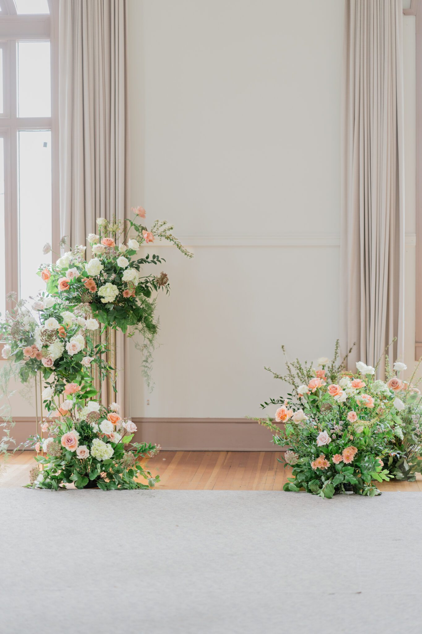 Timeless elegant wedding at Chilliwack Museum in front of ceremony arch with cascading floral arrangements in white and peach with touches of gold.