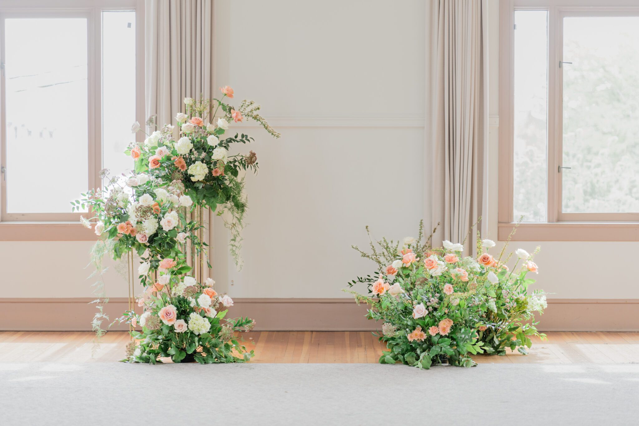 Timeless elegant wedding at Chilliwack Museum in front of ceremony arch with cascading floral arrangements in white and peach with touches of gold. 