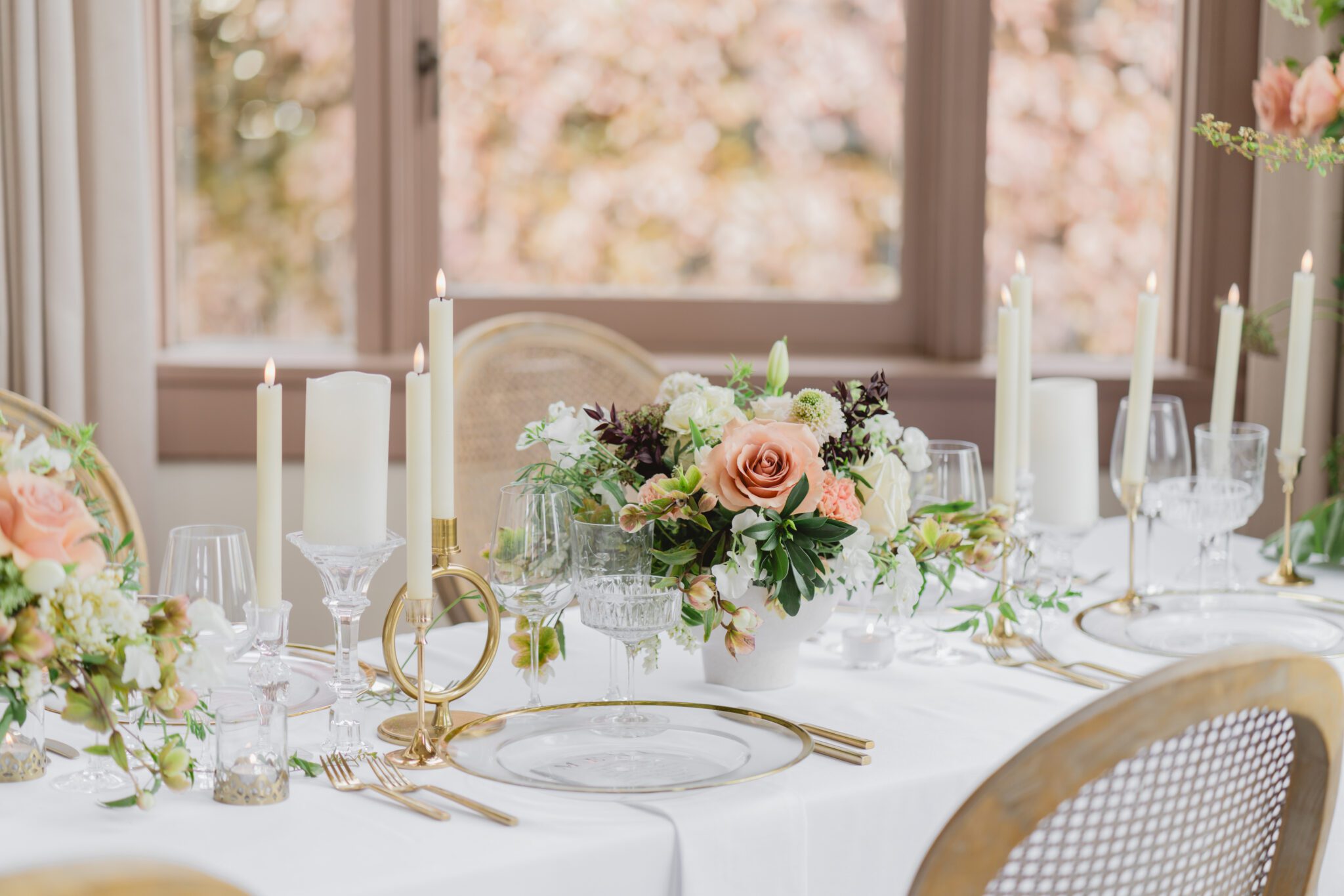 Wedding reception table at Chilliwack Museum, adorned with luxurious gold cutlery, unique candleholders, and vintage-inspired glasses, complemented the cane back chairs. Cascading floral centrepiece and arrangements in white and peach.