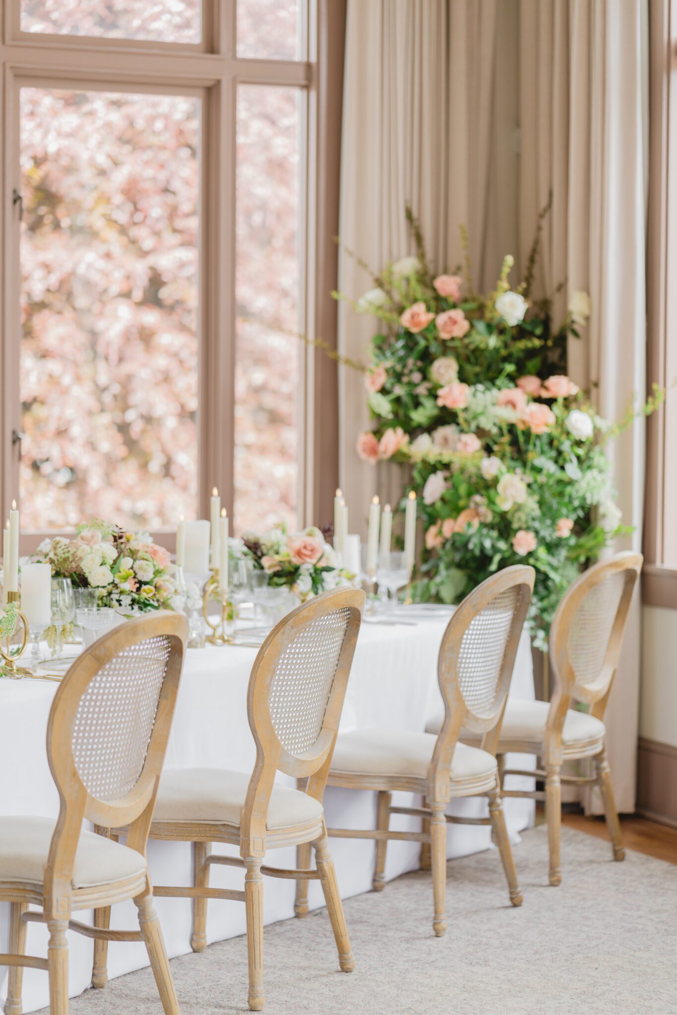 Wedding reception table at Chilliwack Museum, adorned with luxurious gold cutlery, unique candleholders, and vintage-inspired glasses, complemented the cane back chairs. Cascading floral centrepiece and arrangements in white and peach.