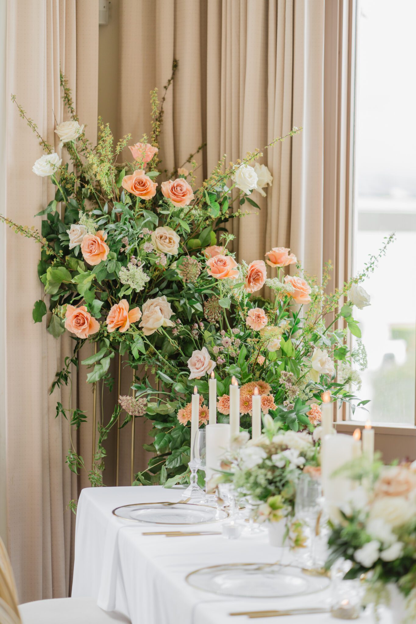 Wedding reception table at Chilliwack Museum, adorned with luxurious gold cutlery, unique candleholders, and vintage-inspired glasses, complemented the cane back chairs. Cascading floral centrepiece and arrangements in white and peach.