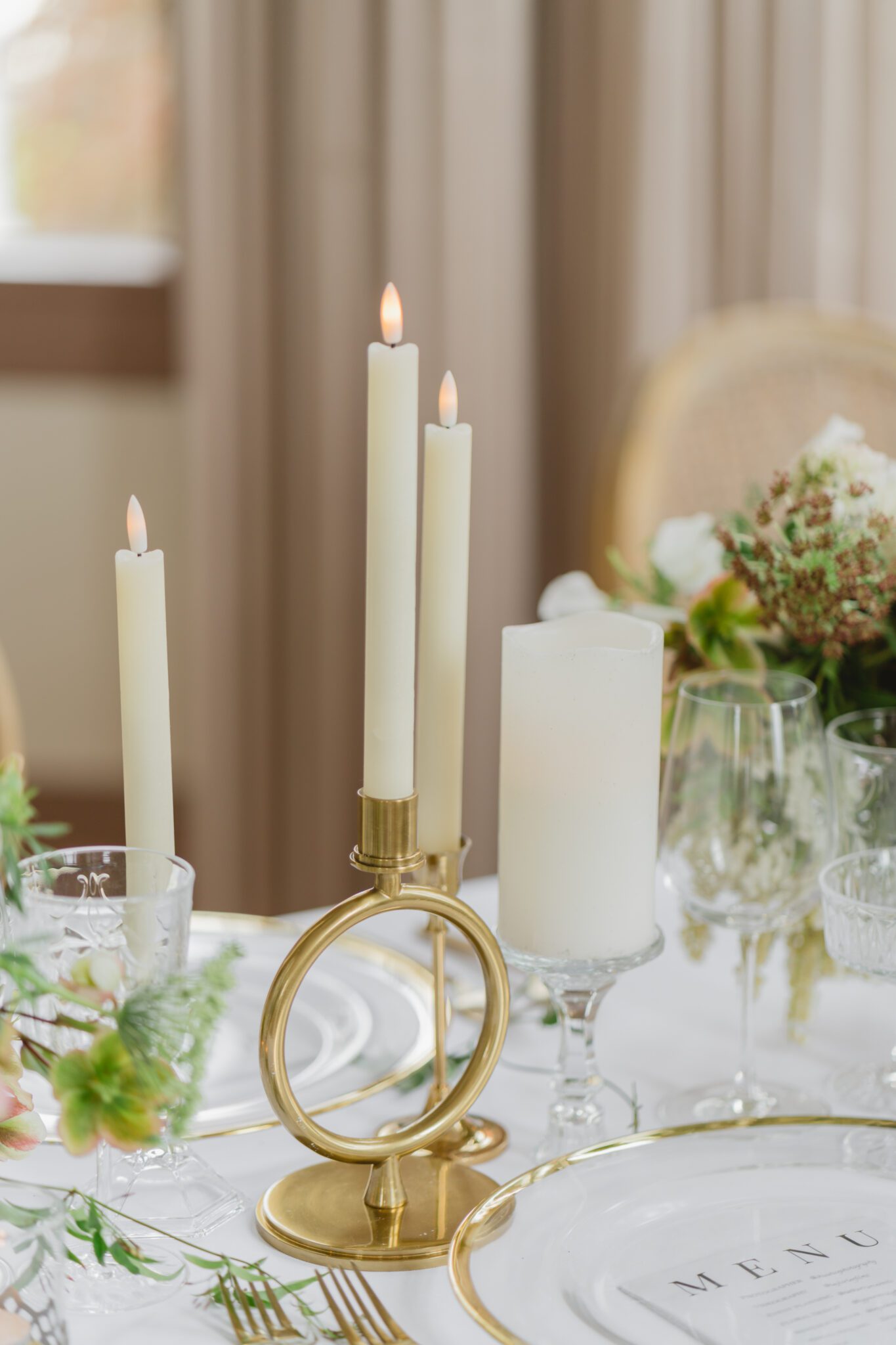 Wedding reception table at Chilliwack Museum, adorned with luxurious gold cutlery, unique candleholders, and vintage-inspired glasses, complemented the cane back chairs. Cascading floral centrepiece and arrangements in white and peach.