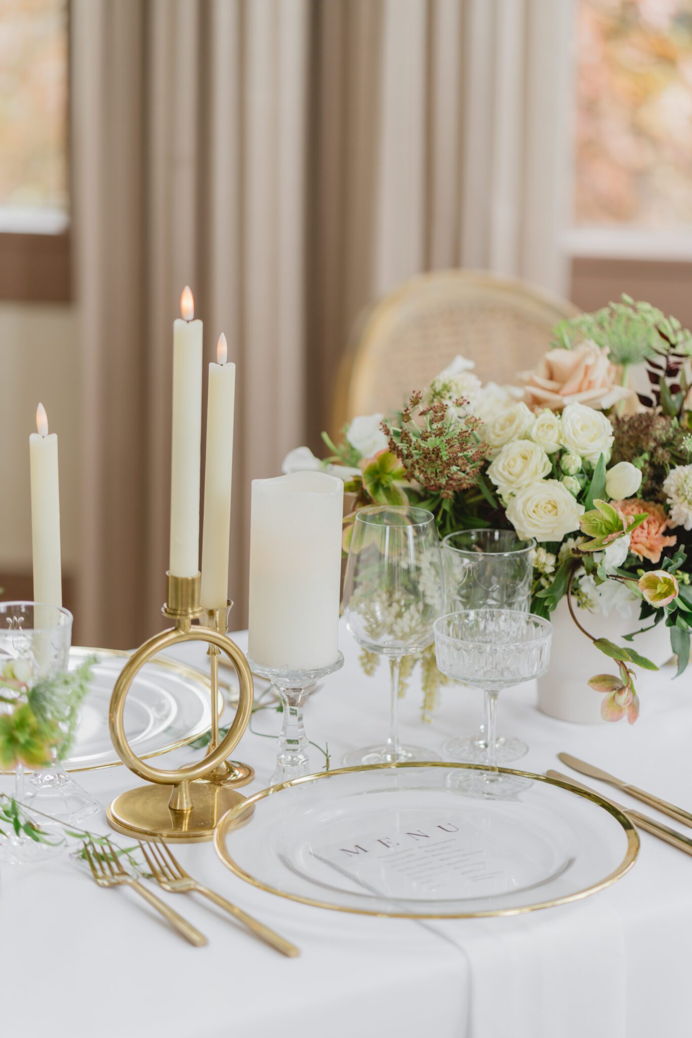 Wedding reception table at Chilliwack Museum, adorned with luxurious gold cutlery, unique candleholders, and vintage-inspired glasses, complemented the cane back chairs. Cascading floral centrepiece and arrangements in white and peach.