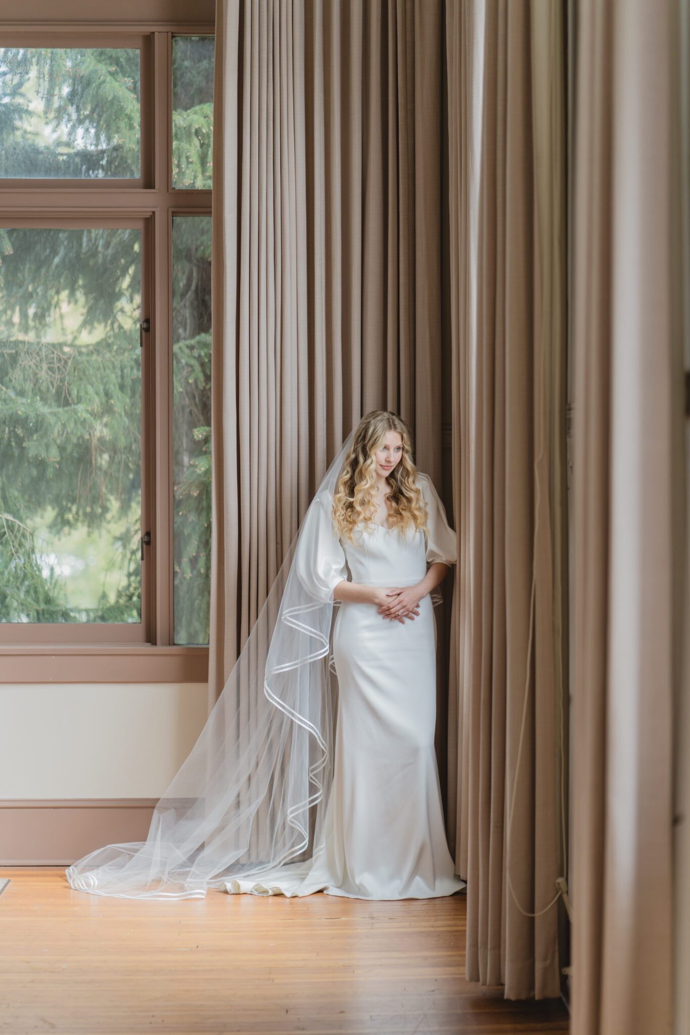 Bride at an elegant wedding at Chilliwack Museum in front of ceremony arch with cascading floral arrangements in white and peach with touches of gold. Bride wearing an elegant crepe wedding dress with a removable bolero and sweetheart neckline. 
