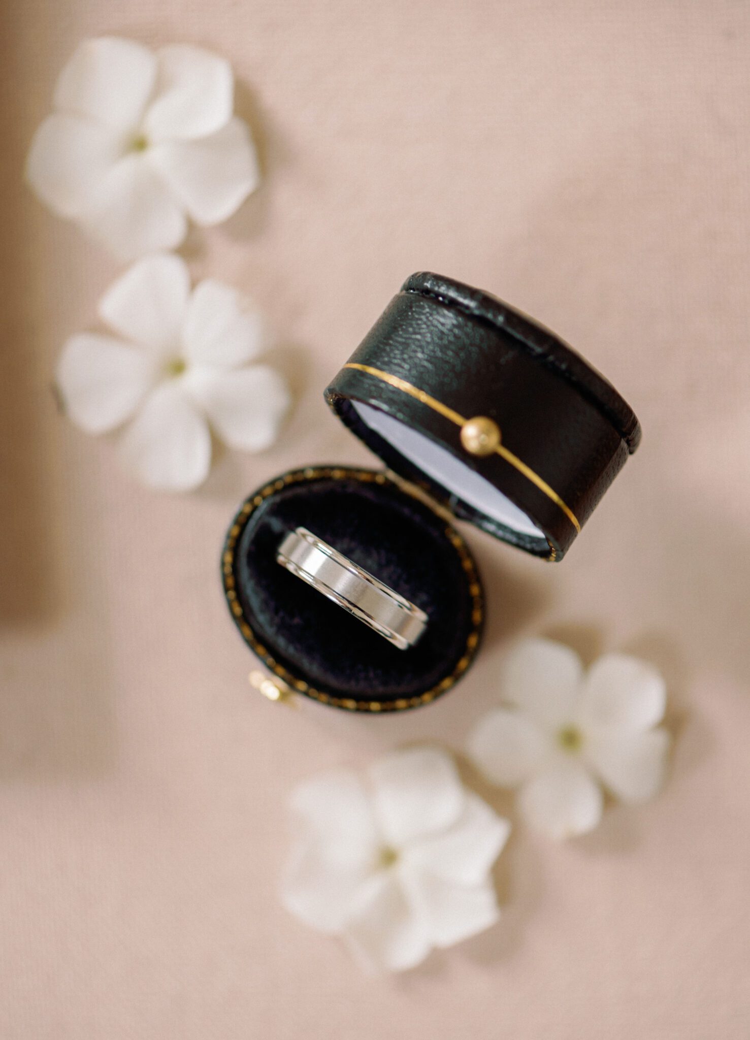 Elegant black ring box with gold detail, surrounded by small white flowers. 