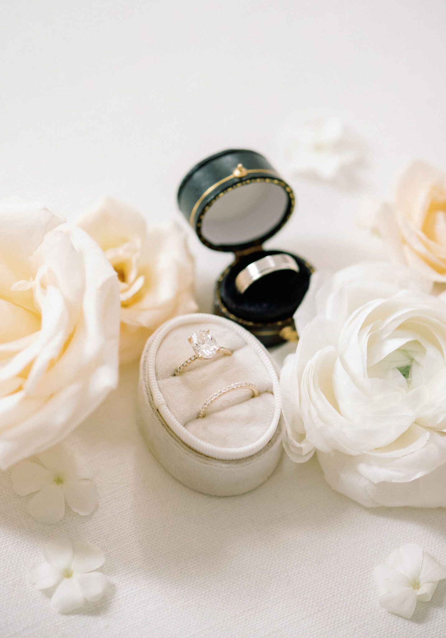 Bride and groom wedding rings in elegant ring boxes surrounded by white and cream roses. 