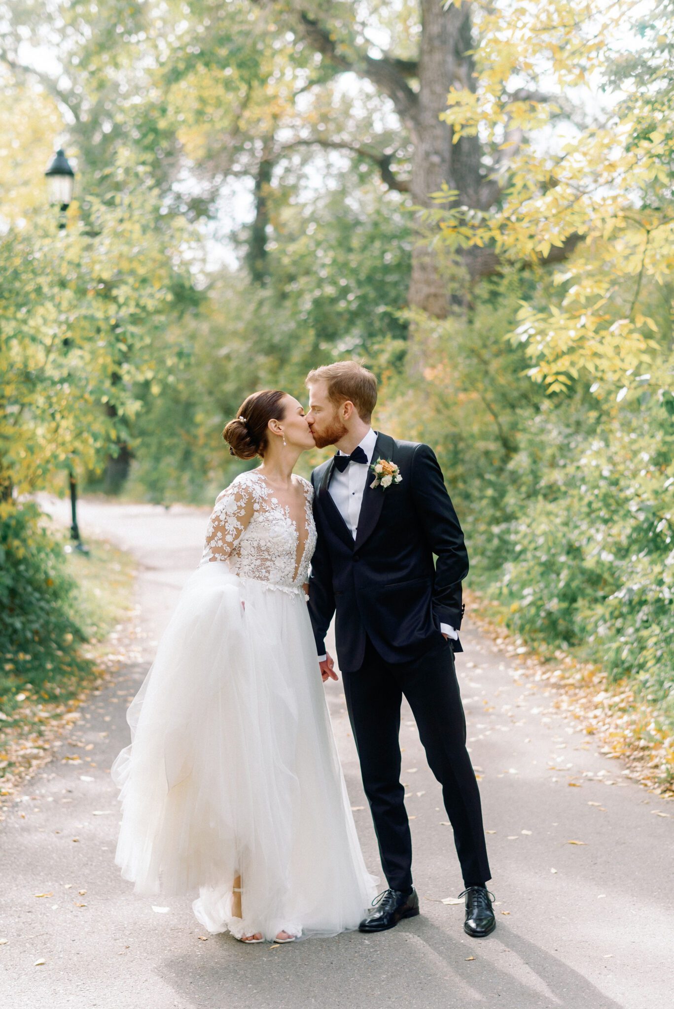 Bride and groom kiss during a romantic wedding portrait session surrounded by trees.