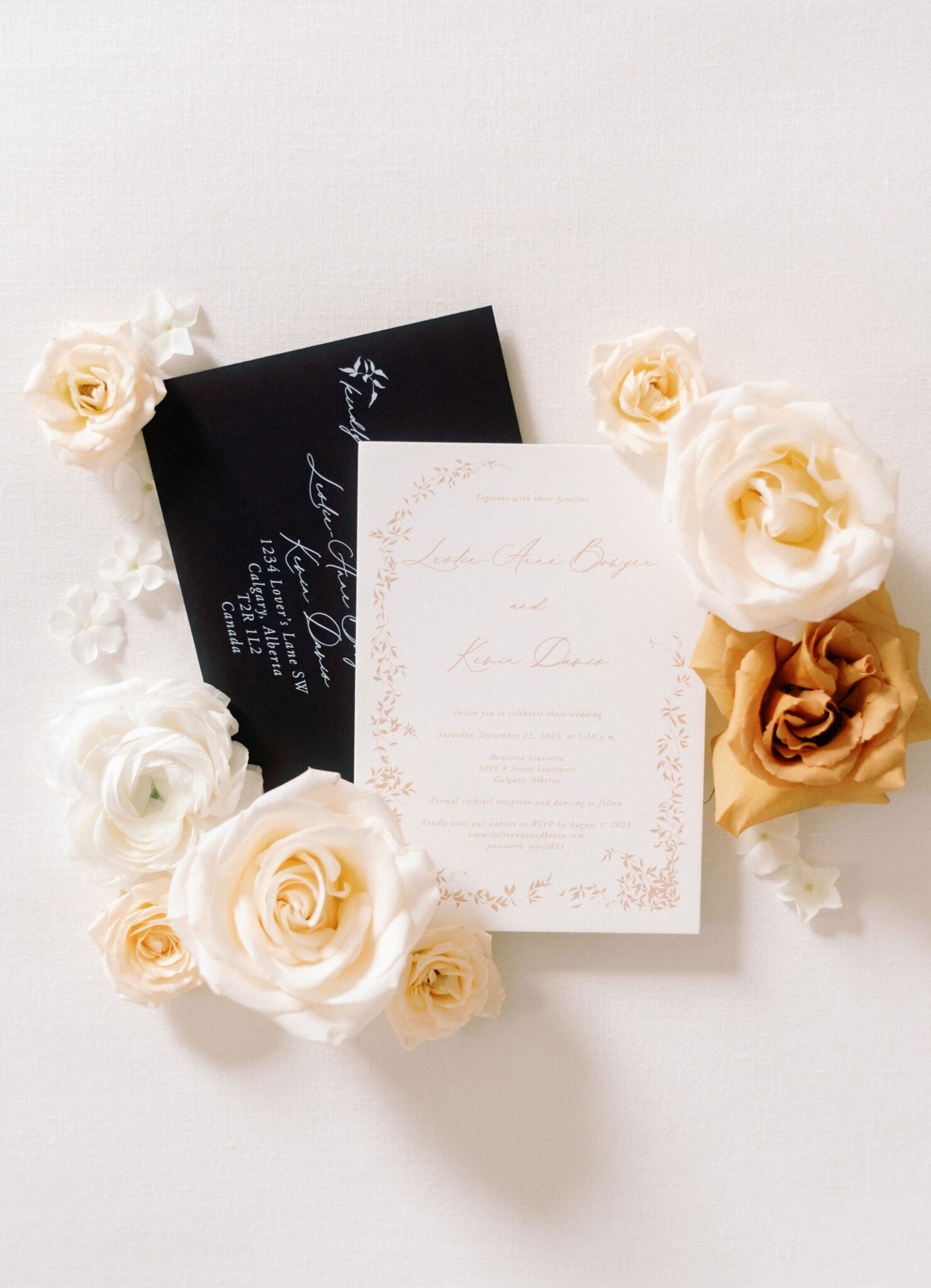 Elegant wedding invitation set with black envelope, gold wax seal, and white floral accents. The invitation features delicate gold leaf details and a formal script, creating a luxurious and timeless design. A diamond engagement ring in a white velvet box and soft white roses complement the stationery, emphasizing a classic, romantic aesthetic.