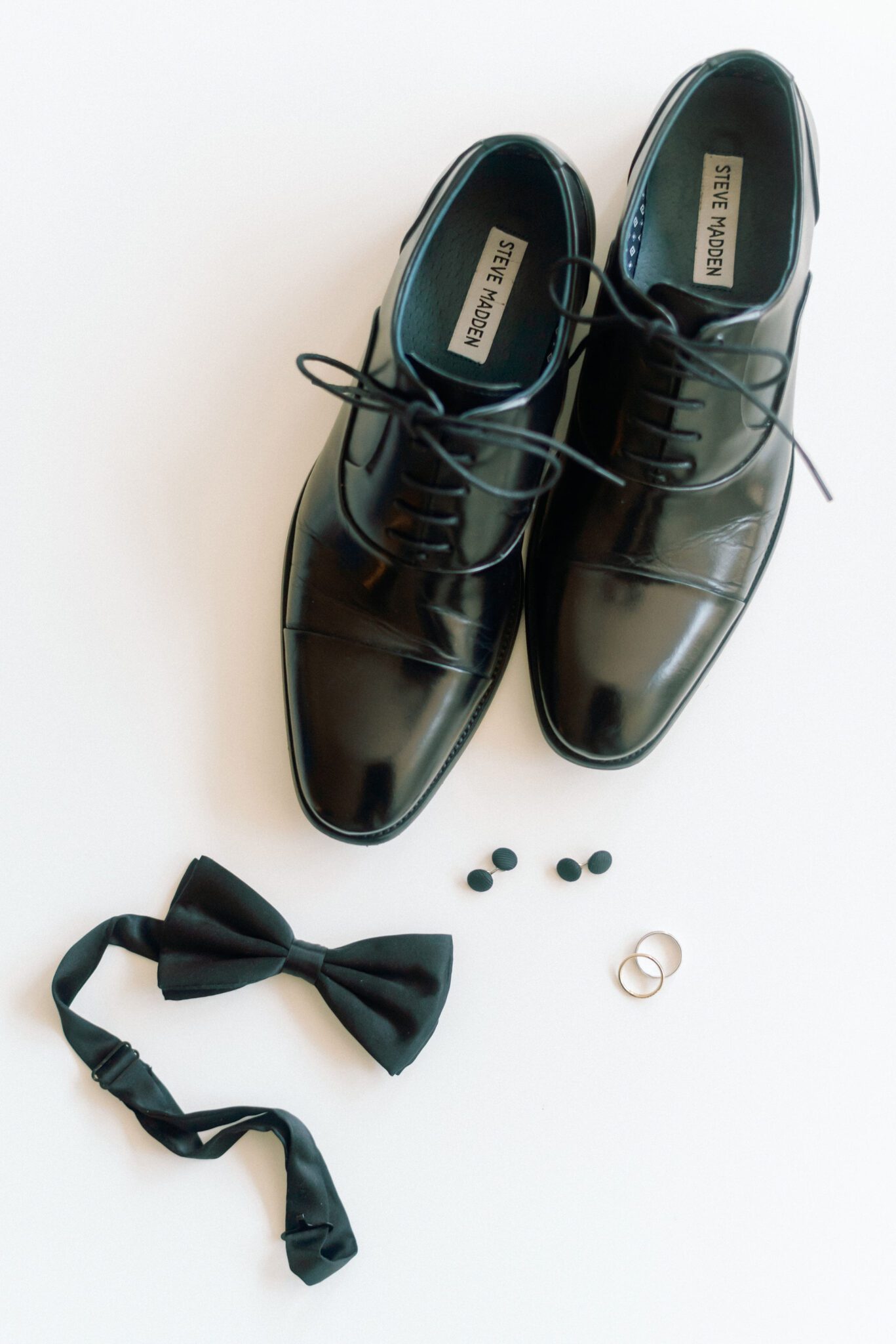 Groom's getting ready details featuring black Steve Madden shoes, black bow tie, cufflinks and wedding rings. 