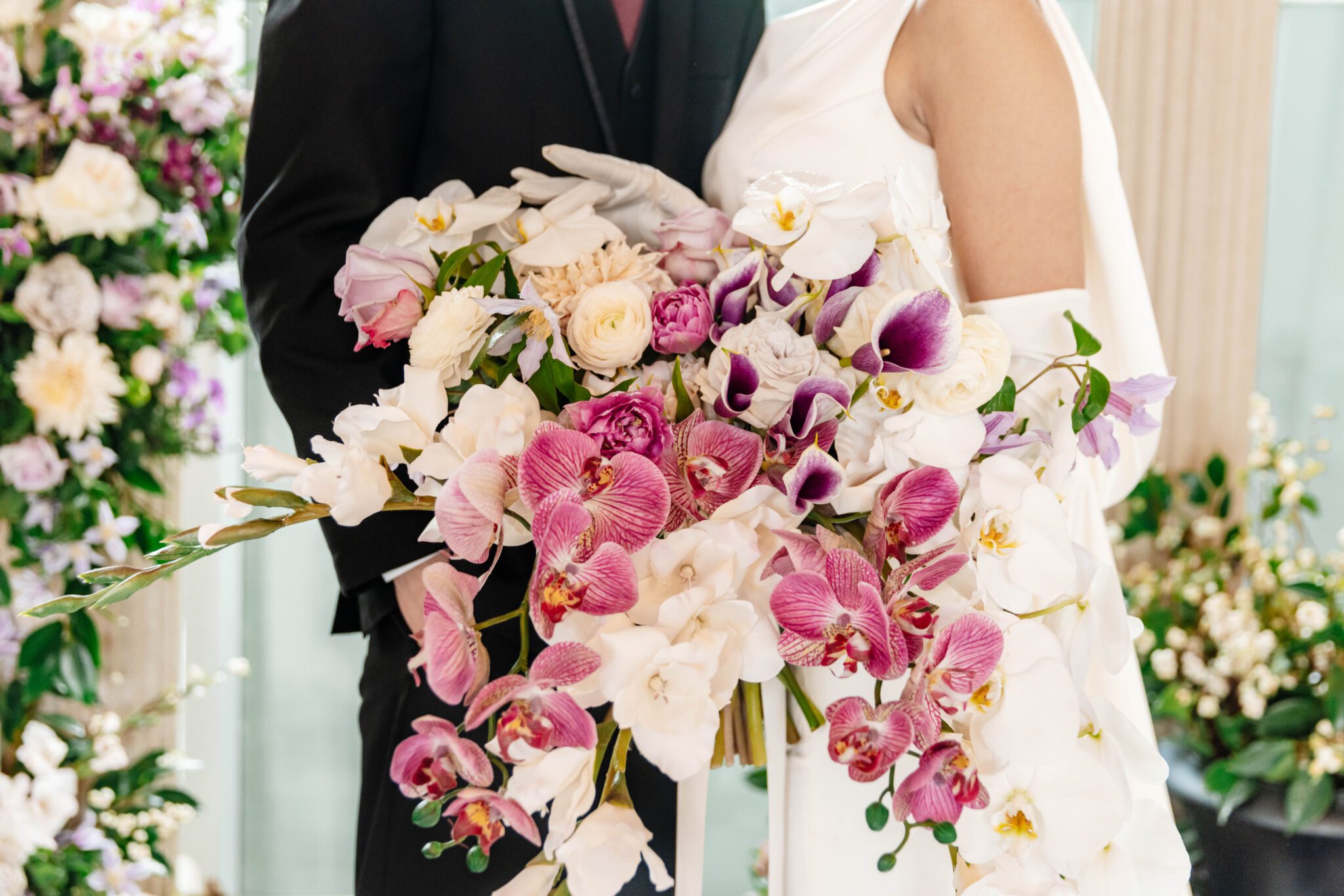 Elegant bride holding a stunning bridal bouquet of purple and white orchids, gladiolas, and purple garden flowers. 