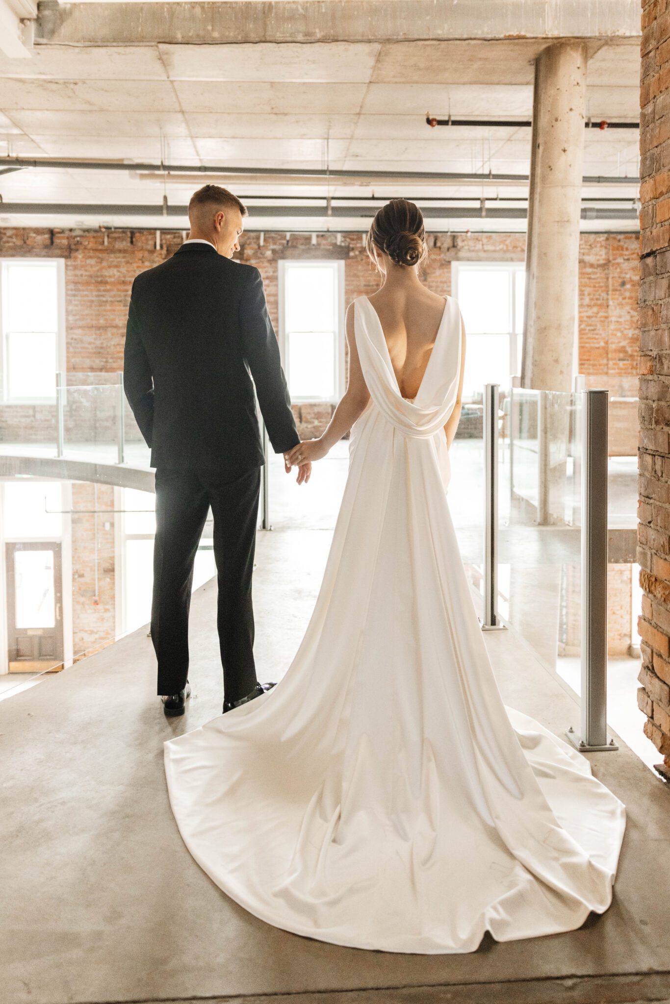 Sophisticated couple walking into reception at historic venue The Pendennis in Edmonton, Alberta. Bride wearing a sleek bridal gown with draping fabric in the back. 