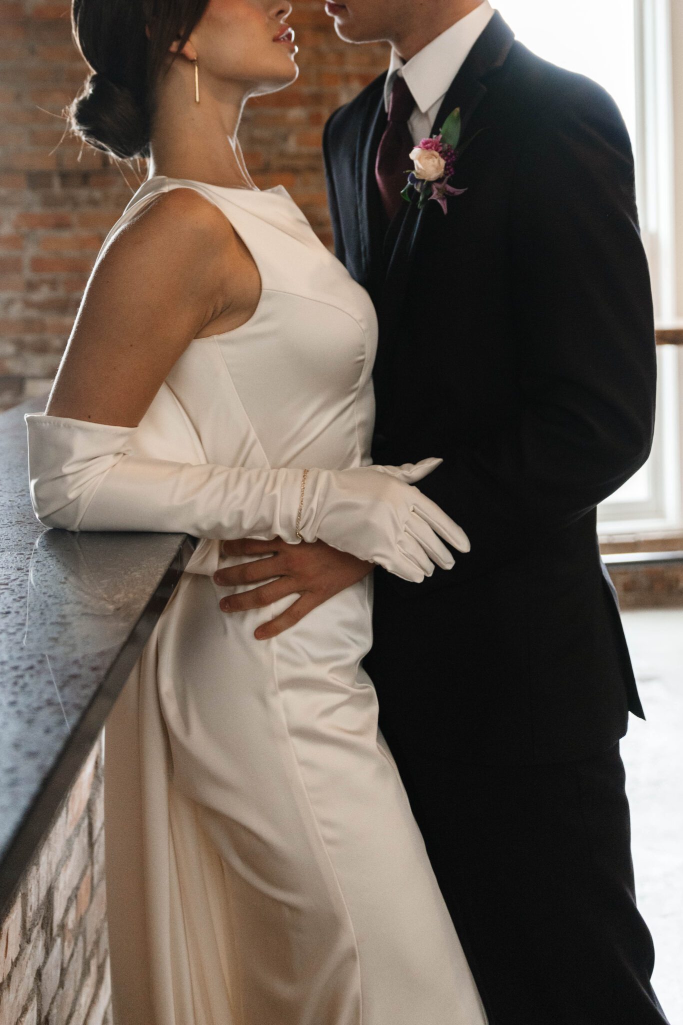 Sophisticated couple embracing during garden-inspired wedding at historic venue The Pendennis in Edmonton, Alberta. Bride wearing a sleek bridal gown with draping fabric in the back. 